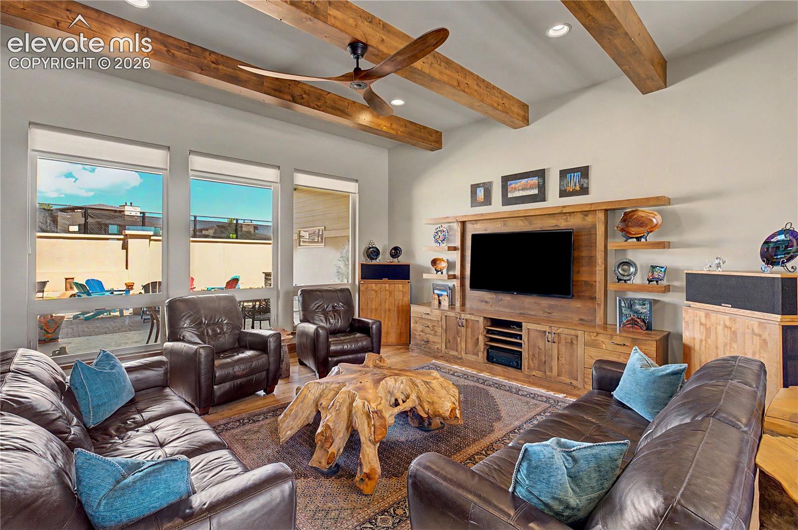 Living room with exposed wood beams, leather seating, and windows overlooking a patio.