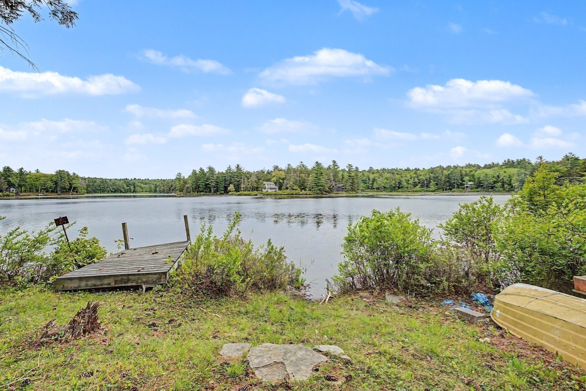 Lakeside property with a wooden dock, grassy shore, and wooded banks across the water.