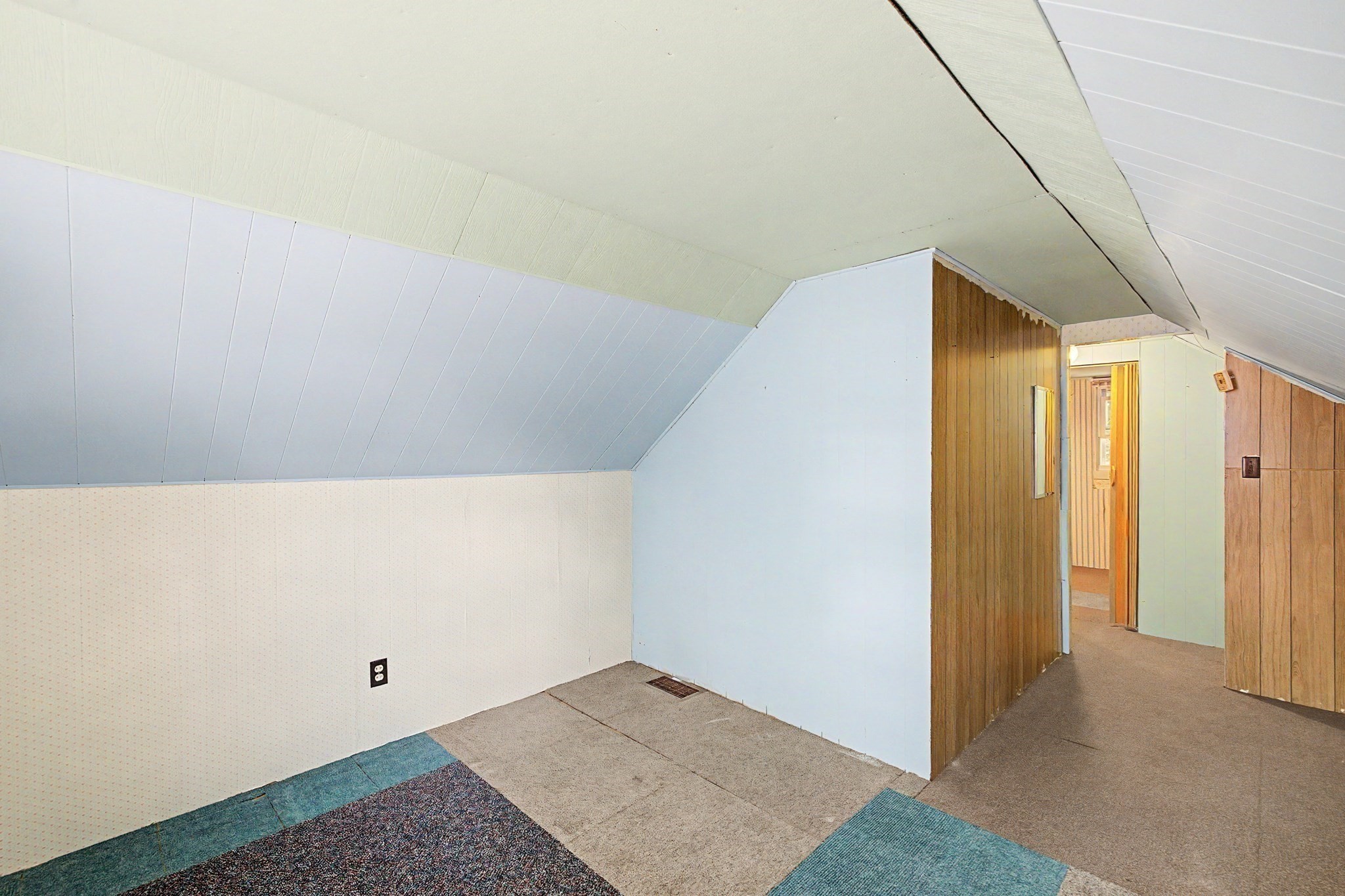 Attic interior with sloped ceilings, carpeted floor, and a wood-paneled hallway.