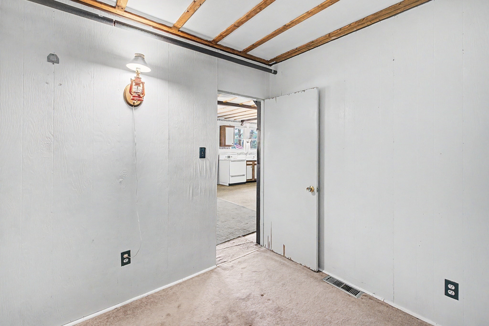 Empty carpeted room with exposed ceiling beams and an open doorway to the kitchen.