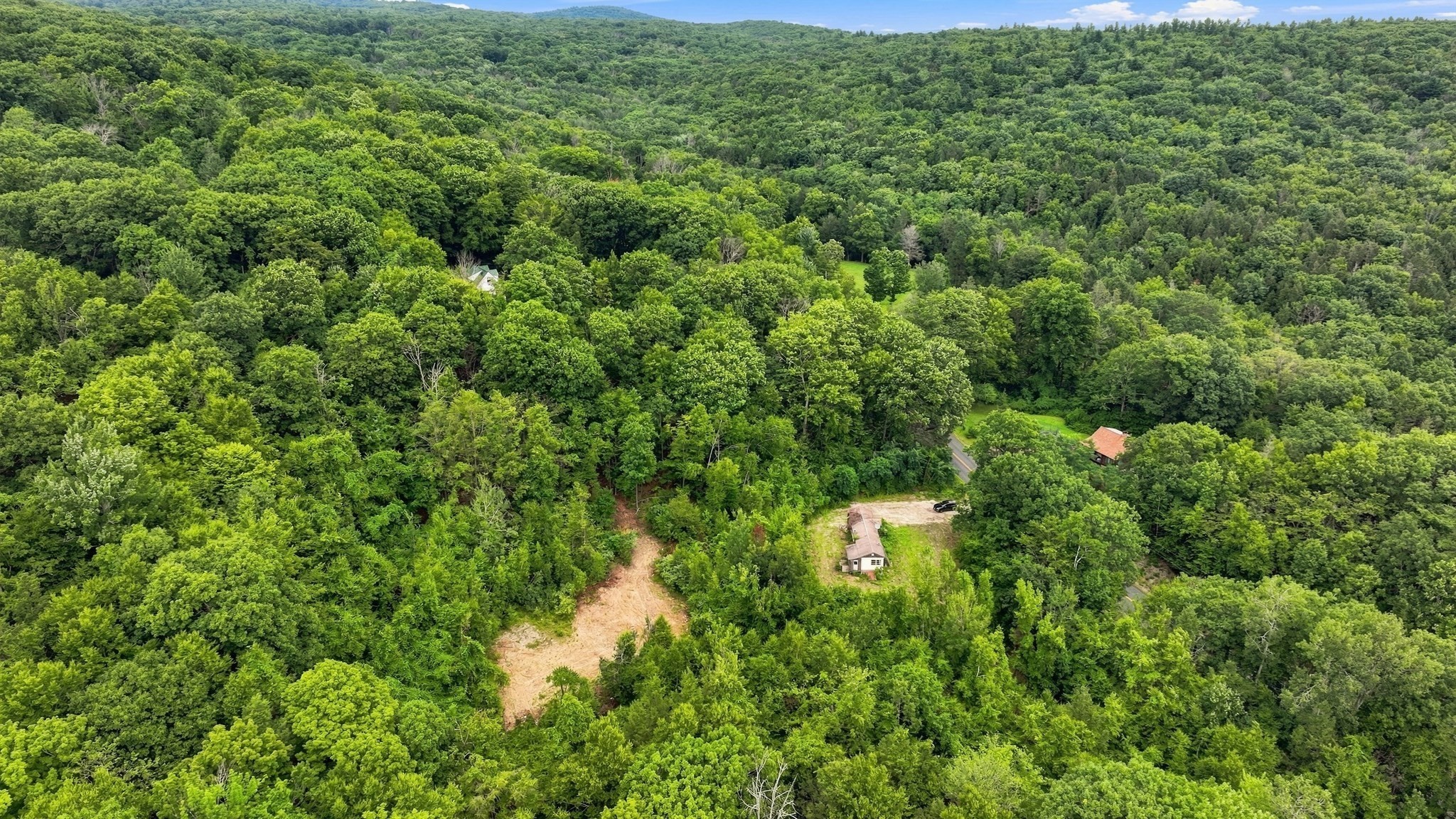 Aerial view of a forested property with a clearing, small building, and winding driveway.
