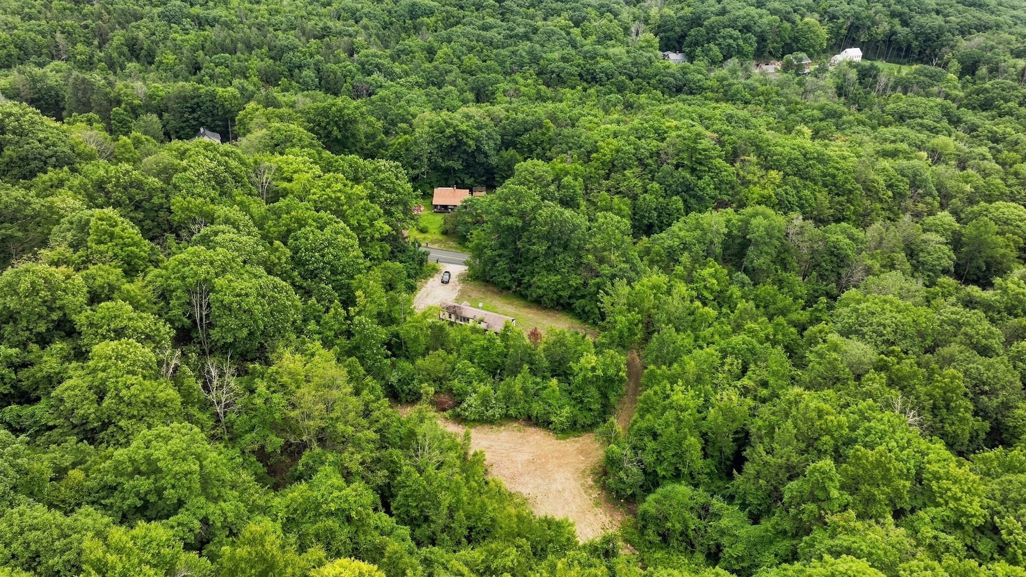 Aerial view of a wooded property with scattered buildings and a broad cleared driveway.