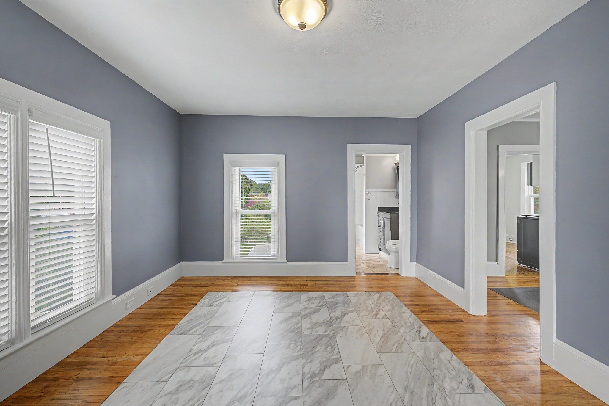 Empty gray-walled room with hardwood floors, a marble-look tile inset, and a bathroom doorway.