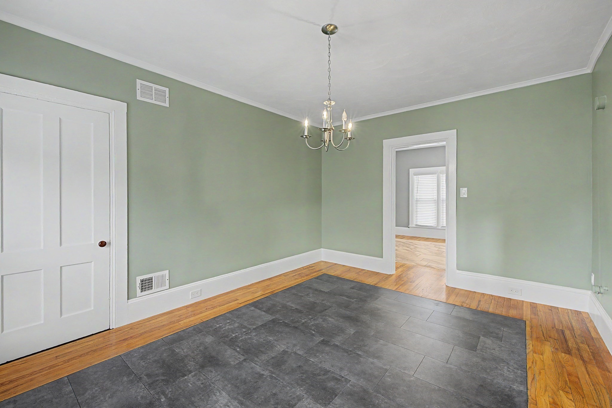 Empty green-walled room with a chandelier and slate tile floor bordered by hardwood.