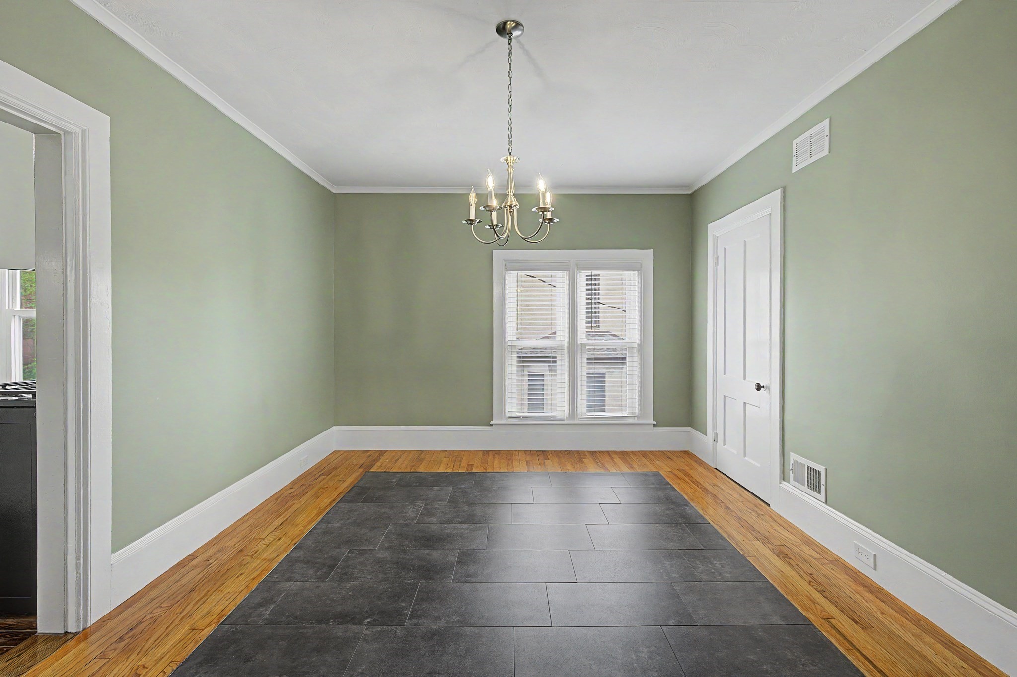 Empty dining room with a chandelier, dark tile flooring bordered by hardwood, and a double window.
