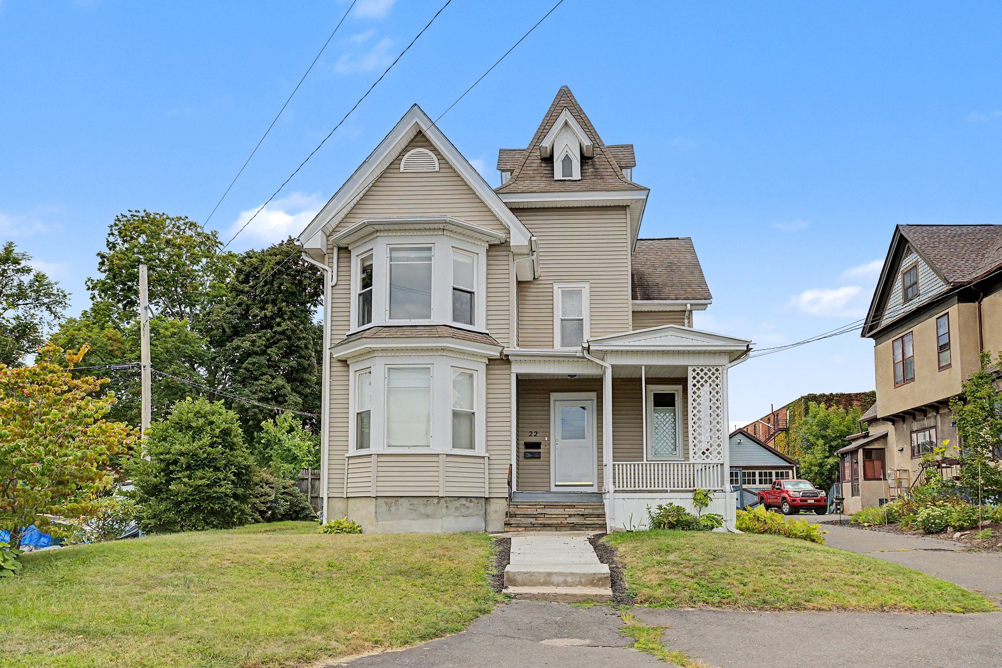 Beige multi-story house with bay windows, steep gables, and a covered front porch.