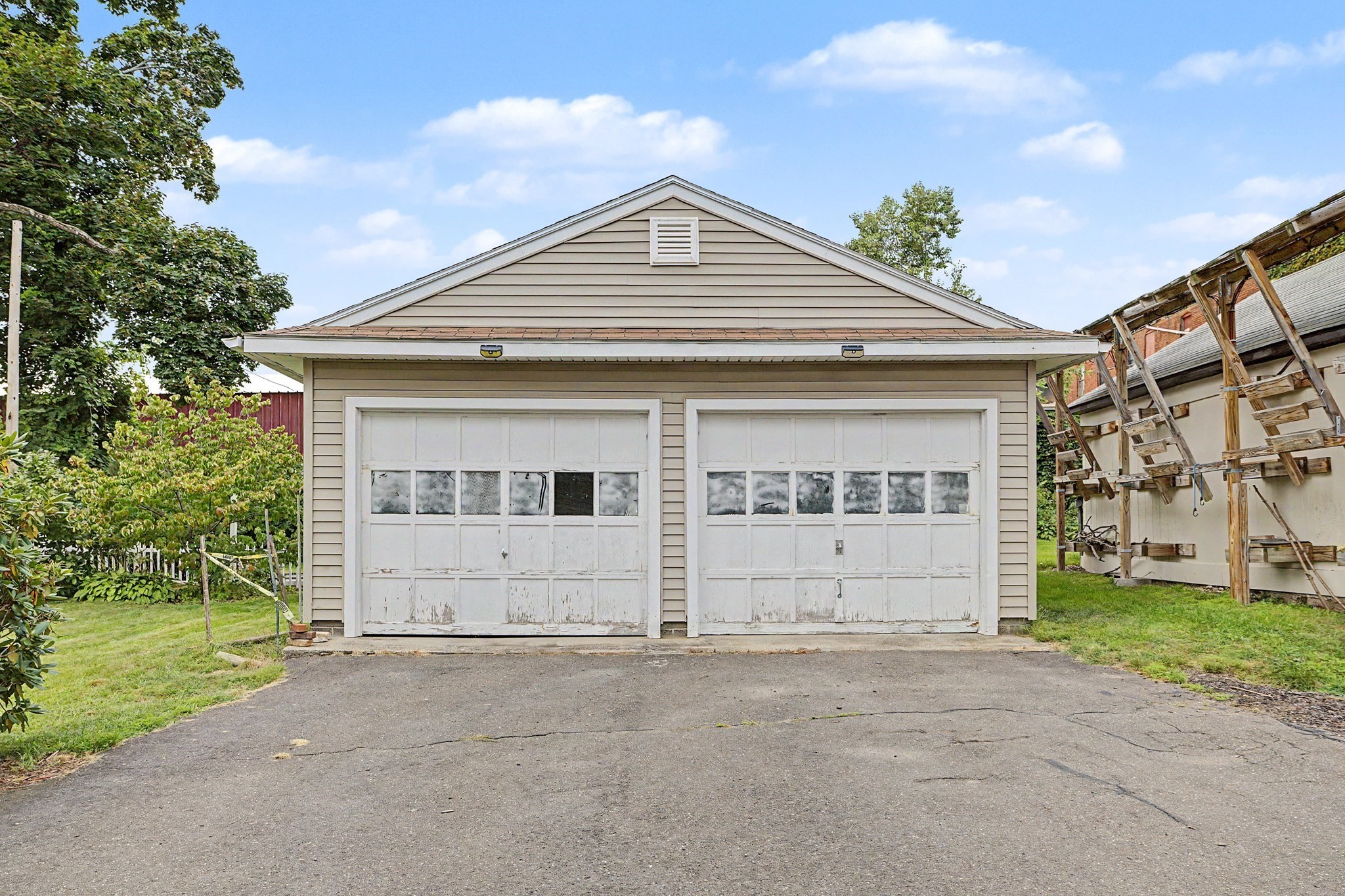 Beige garage with two white doors and a broad paved driveway.