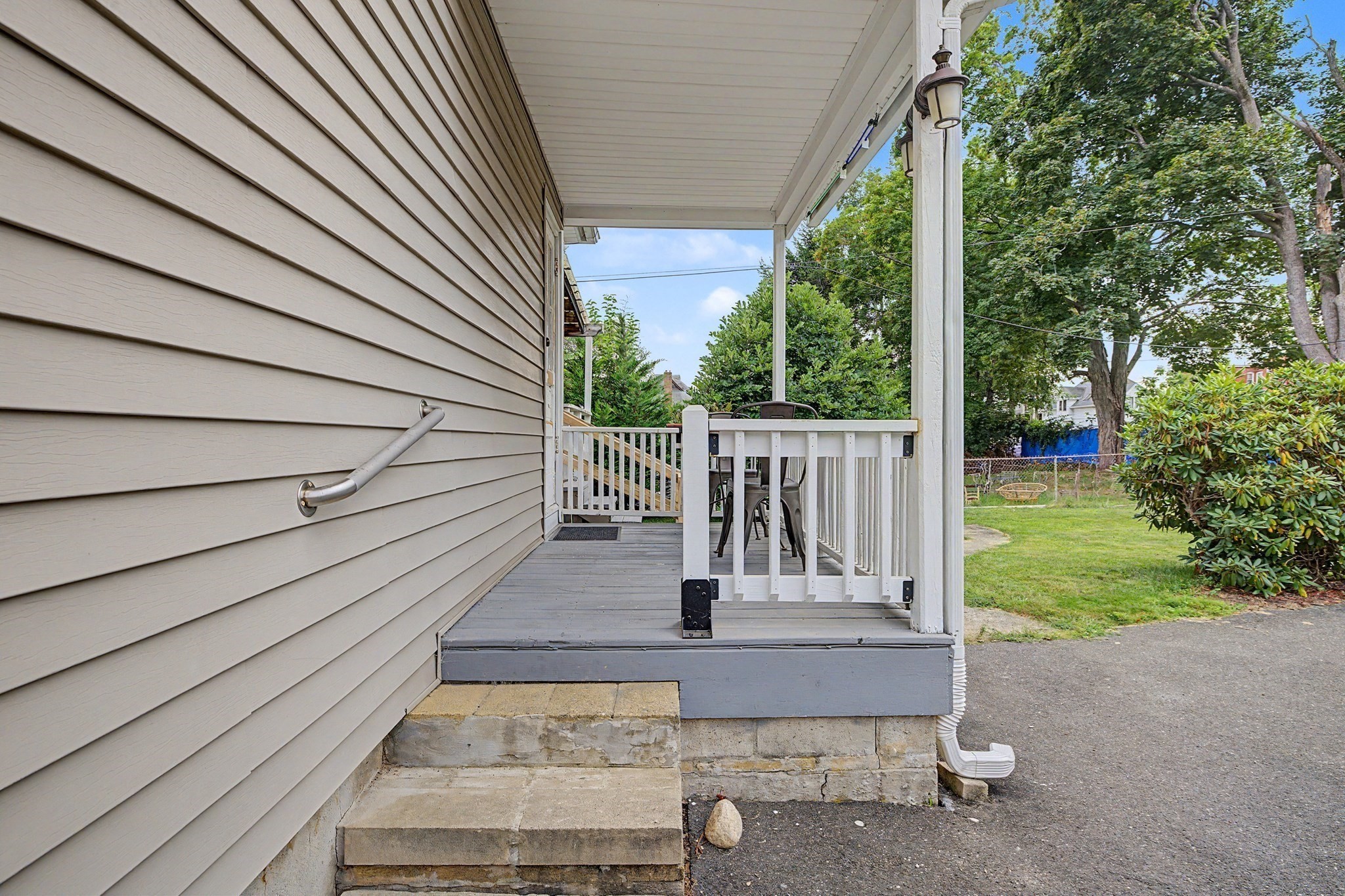 Covered porch with white railings and patio furniture beside a leafy yard.