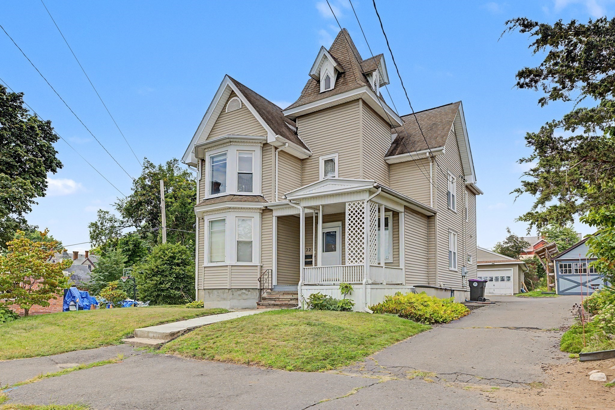 Beige house with a peaked tower, bay windows, and a covered porch beside the driveway.