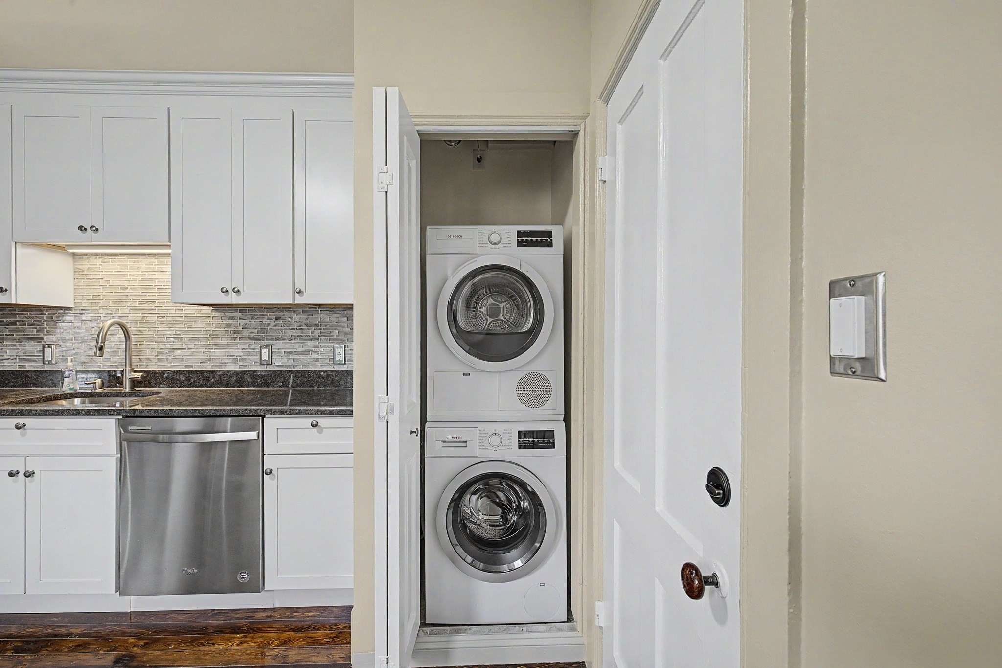 Kitchen with white cabinetry and a closet housing stacked front-loading washer and dryer.
