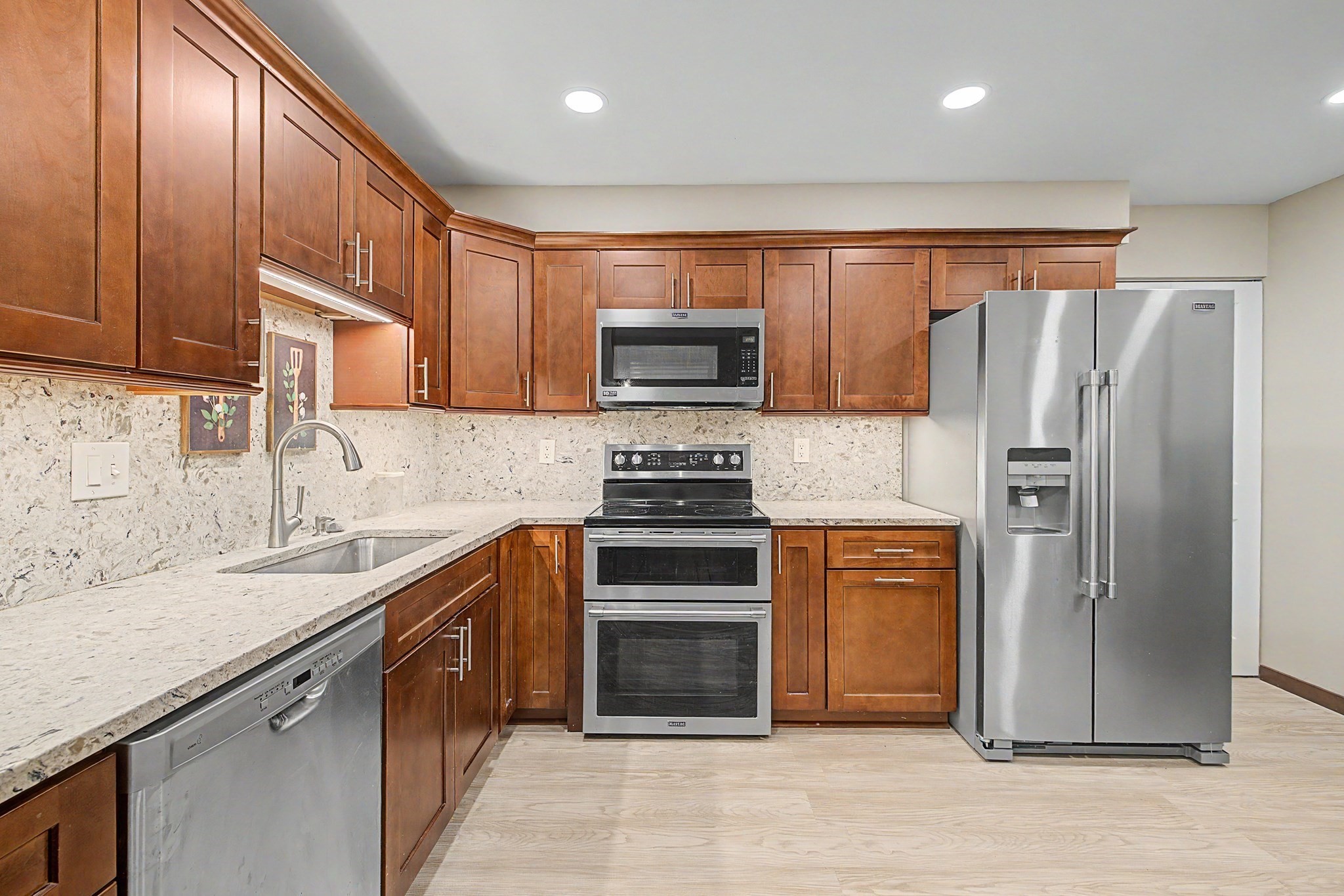 Kitchen with brown wood cabinets, light stone counters, and stainless steel appliances.