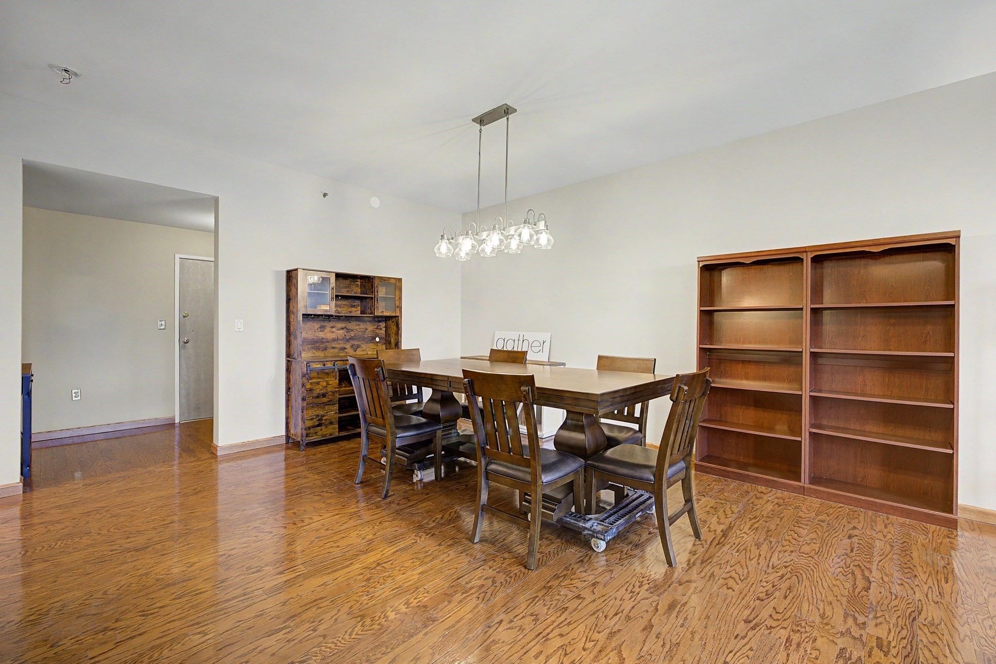 Dining room with a large wooden table, glass chandelier, hardwood floors, and tall bookshelves.