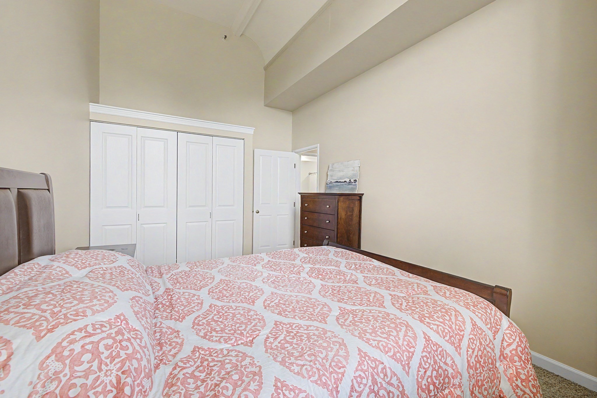 Bedroom with a patterned bedspread, white closet doors, and a dark wood dresser.