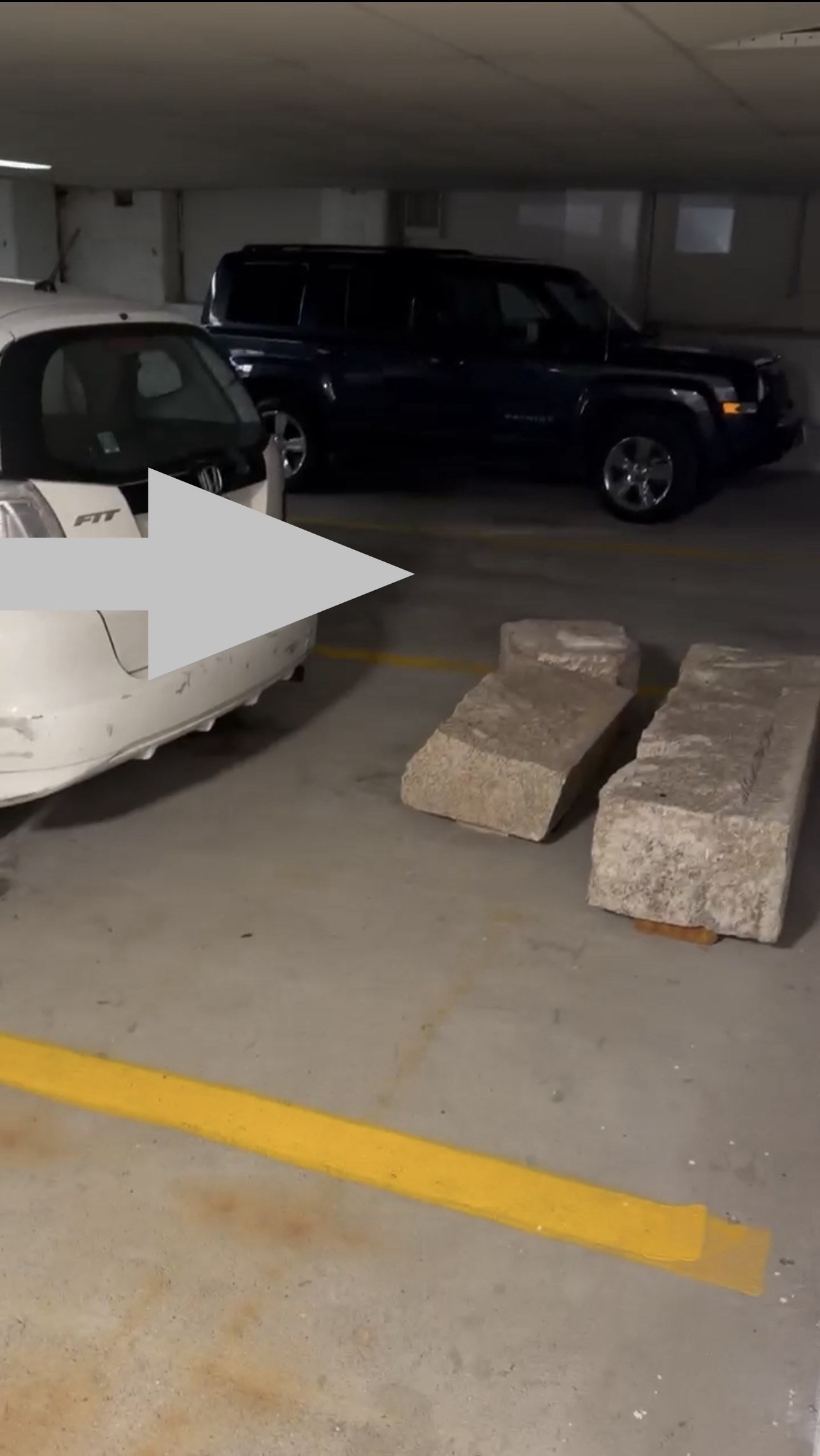 Indoor parking garage with yellow space markings, concrete wheel stops, and parked cars.