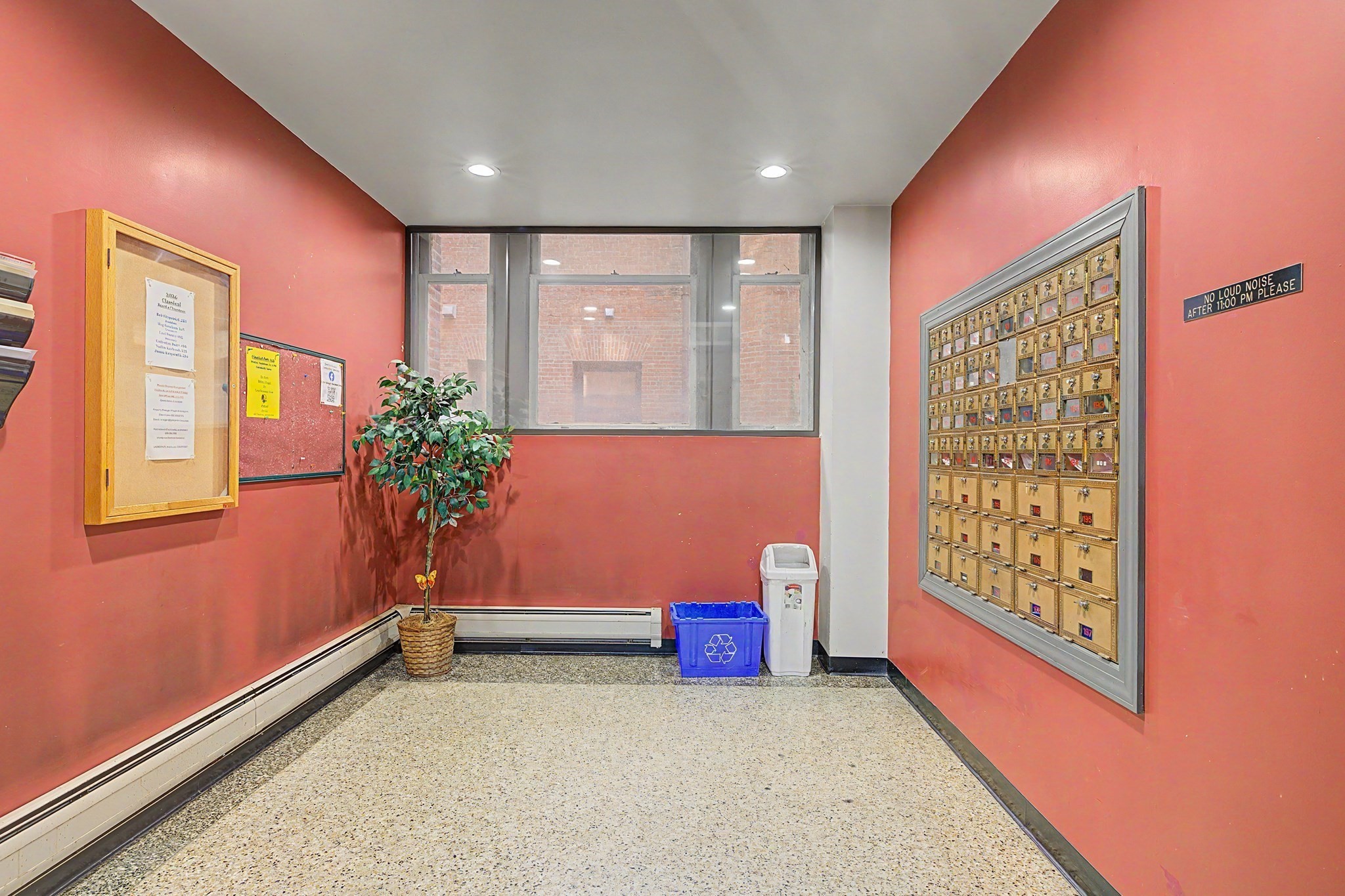 Apartment mailroom with brass mailboxes, red walls, and a window.