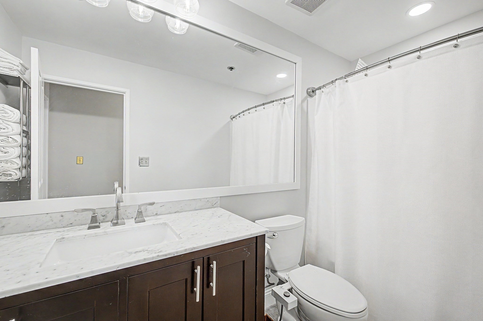 Bathroom with a marble vanity, large mirror, dark wood cabinets, and white shower curtain.