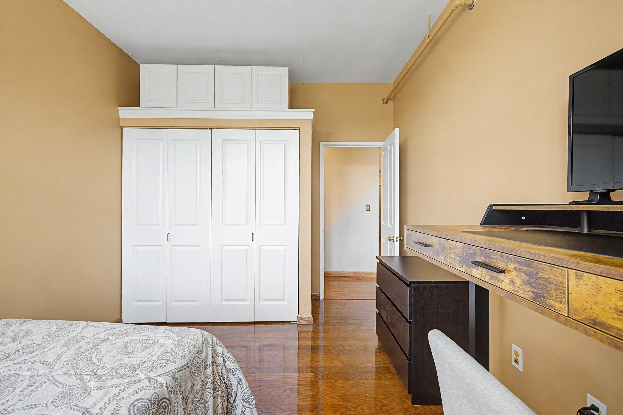 Bedroom with a white built-in wardrobe, hardwood floors, and a wooden dresser topped by a television.