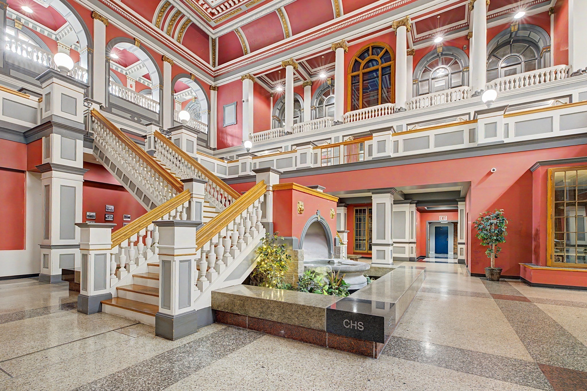 Building lobby with a grand staircase, arched windows, and a central fountain.