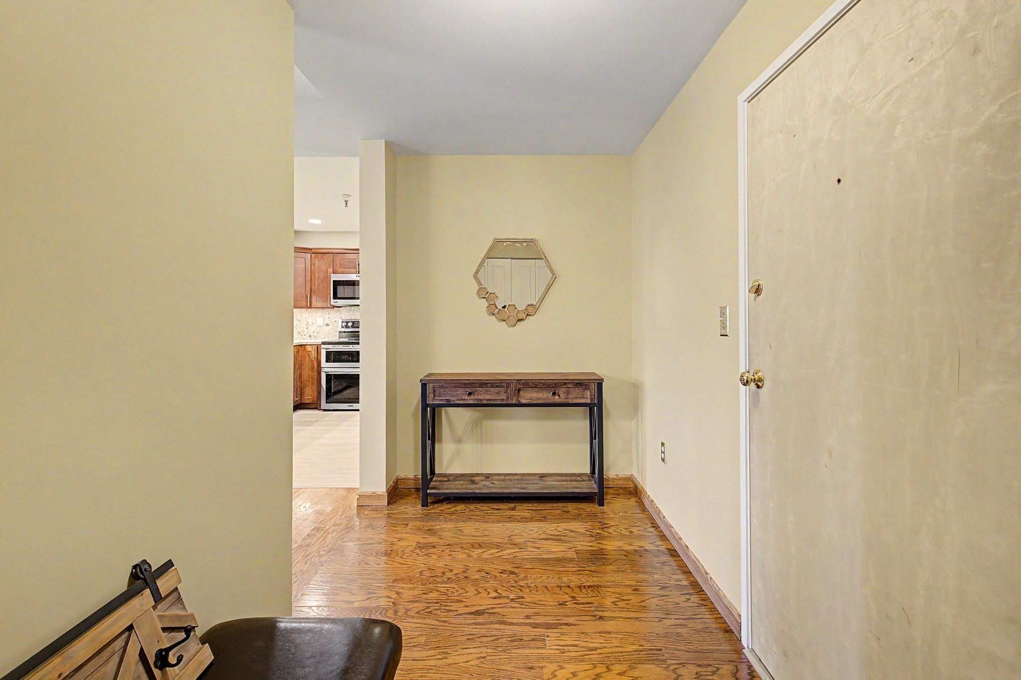 Apartment entry hall with a wood floor, console table, geometric mirror, and a glimpse of the kitchen.