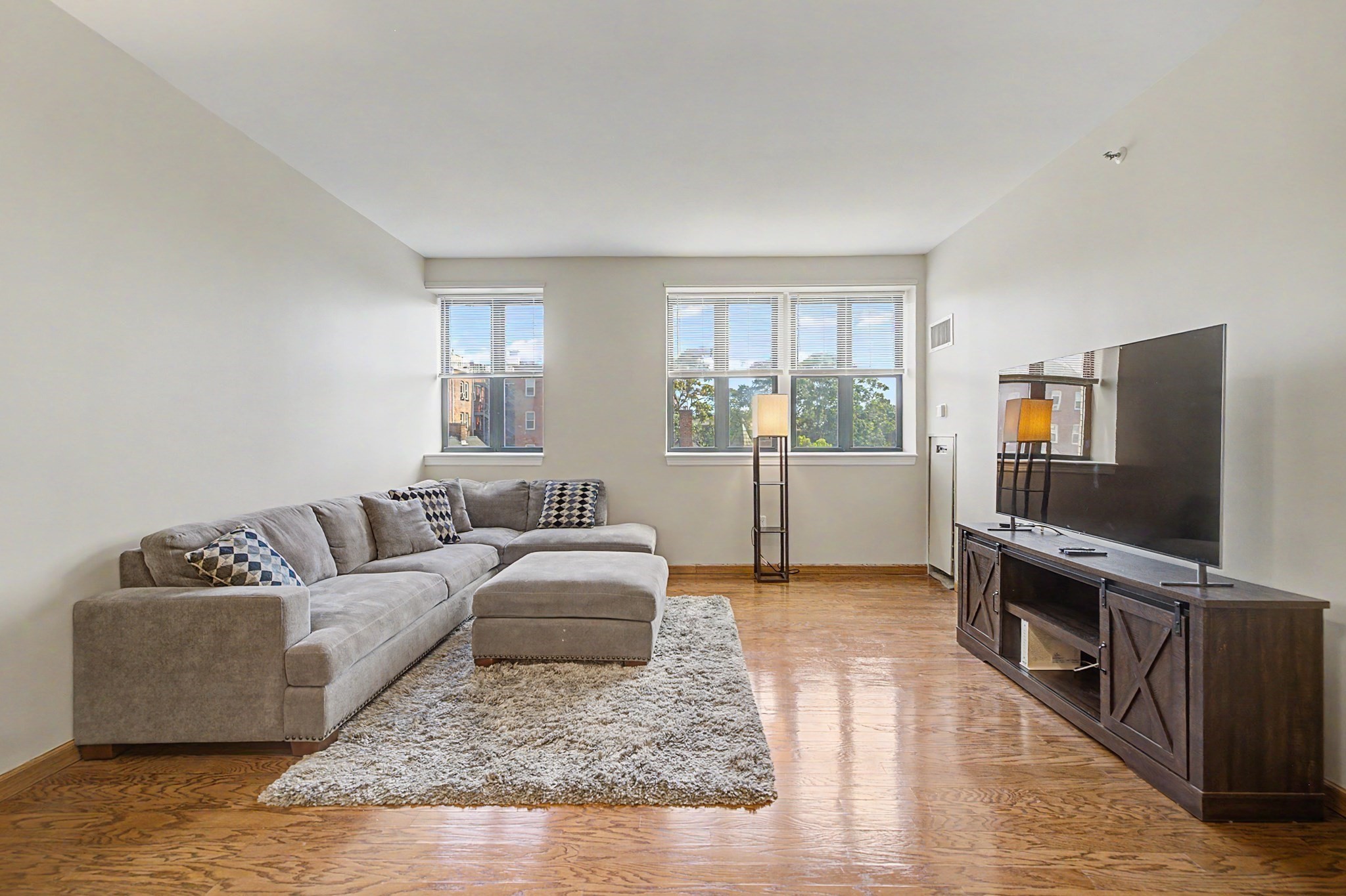 Living room with a gray sectional, hardwood floors, and large windows.