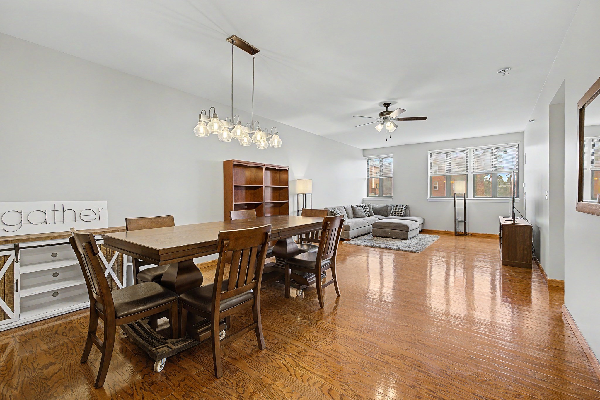 Open-plan dining and living room with a large wooden table, gray sectional, and polished hardwood floors.