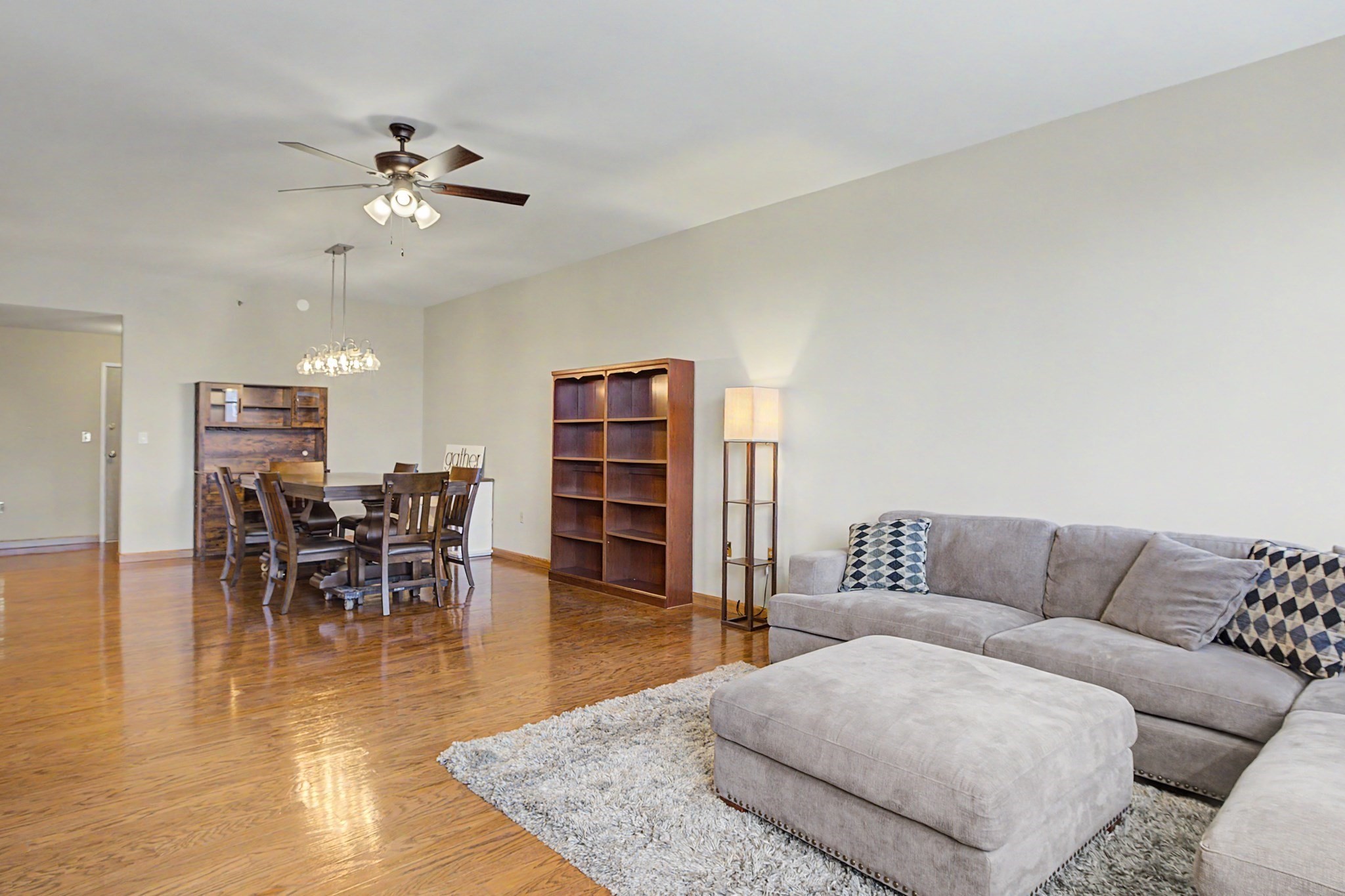 Open-plan living and dining area with a gray sectional, hardwood floors, and a wooden dining set.