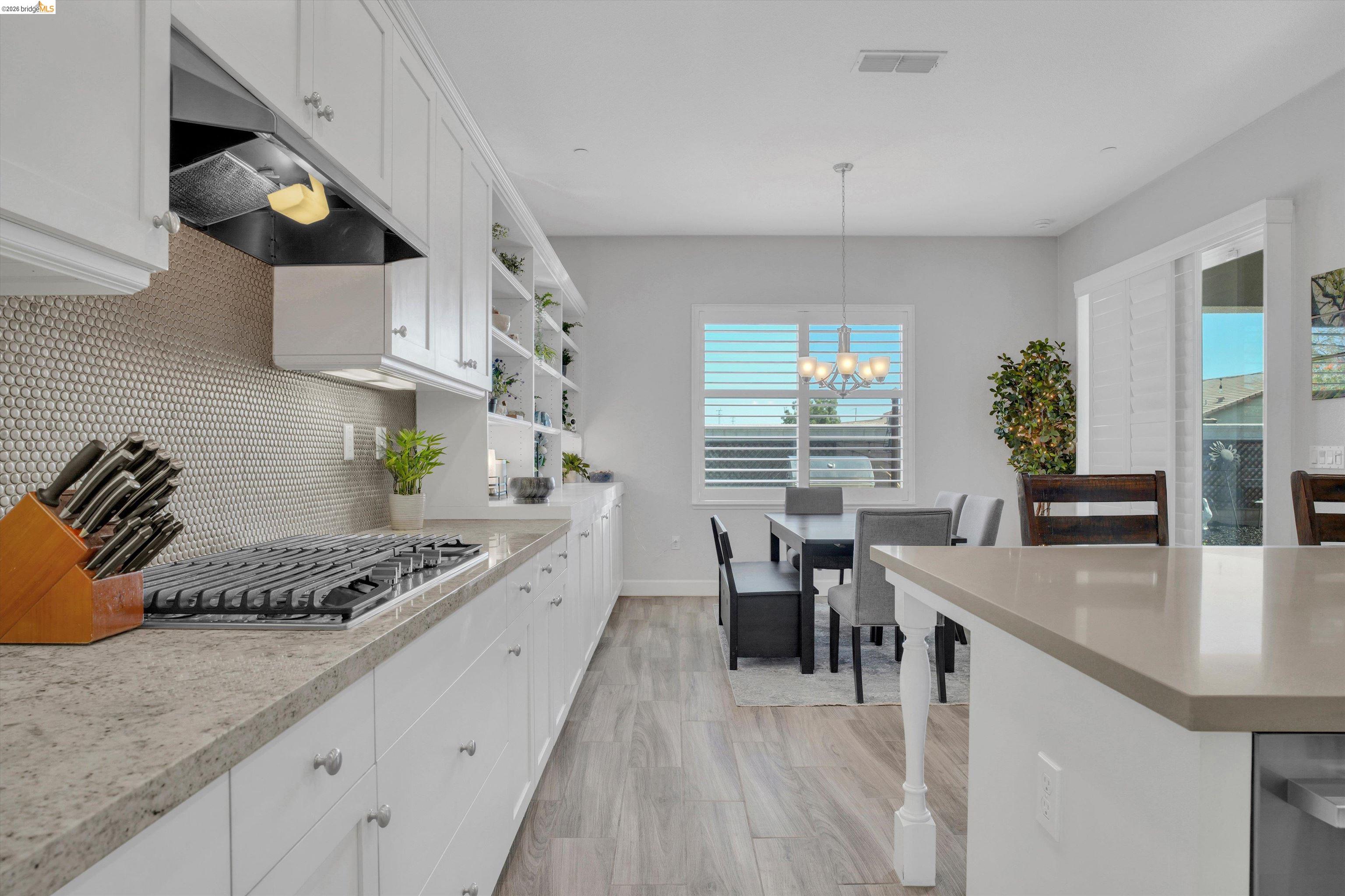 Bright kitchen with white cabinetry, a gas range, mosaic backsplash, and an adjoining dining area.