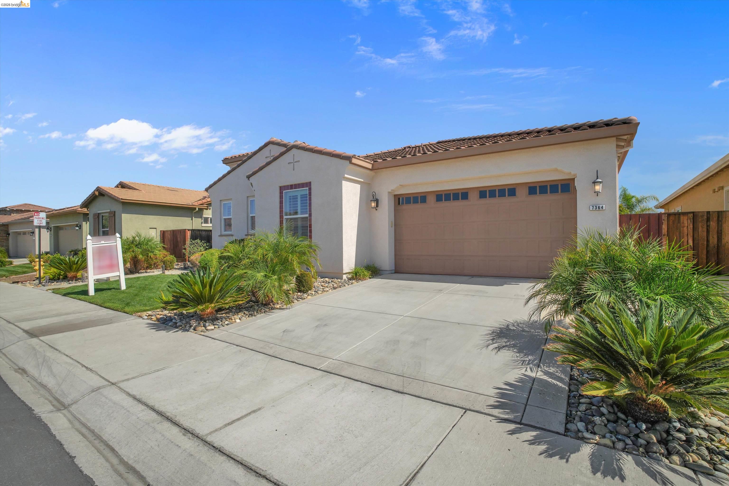Single-story stucco home with a brown garage door, tile roof, and landscaped front yard.