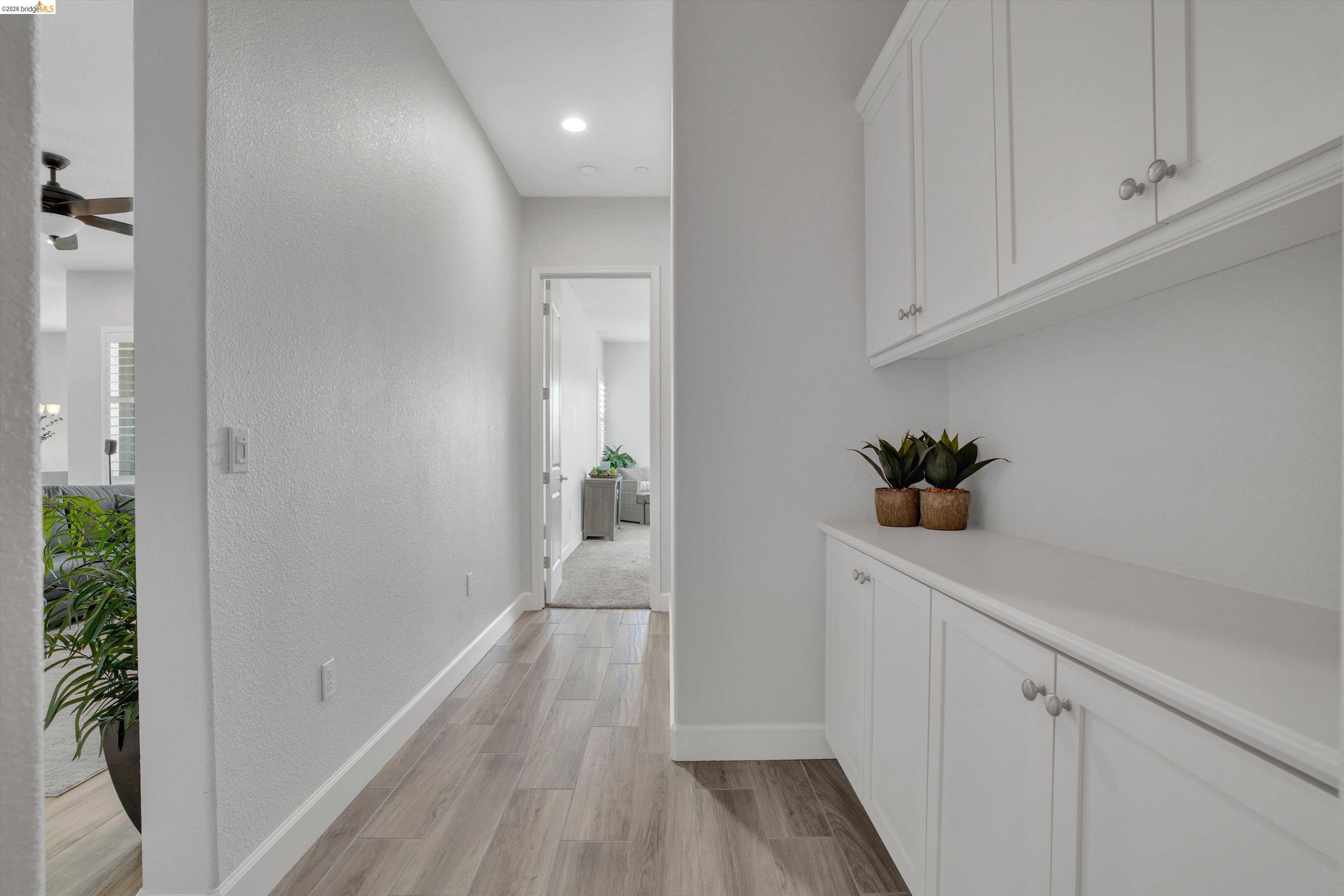 Hallway with white built-in cabinets, wood-look tile flooring, and potted plants.