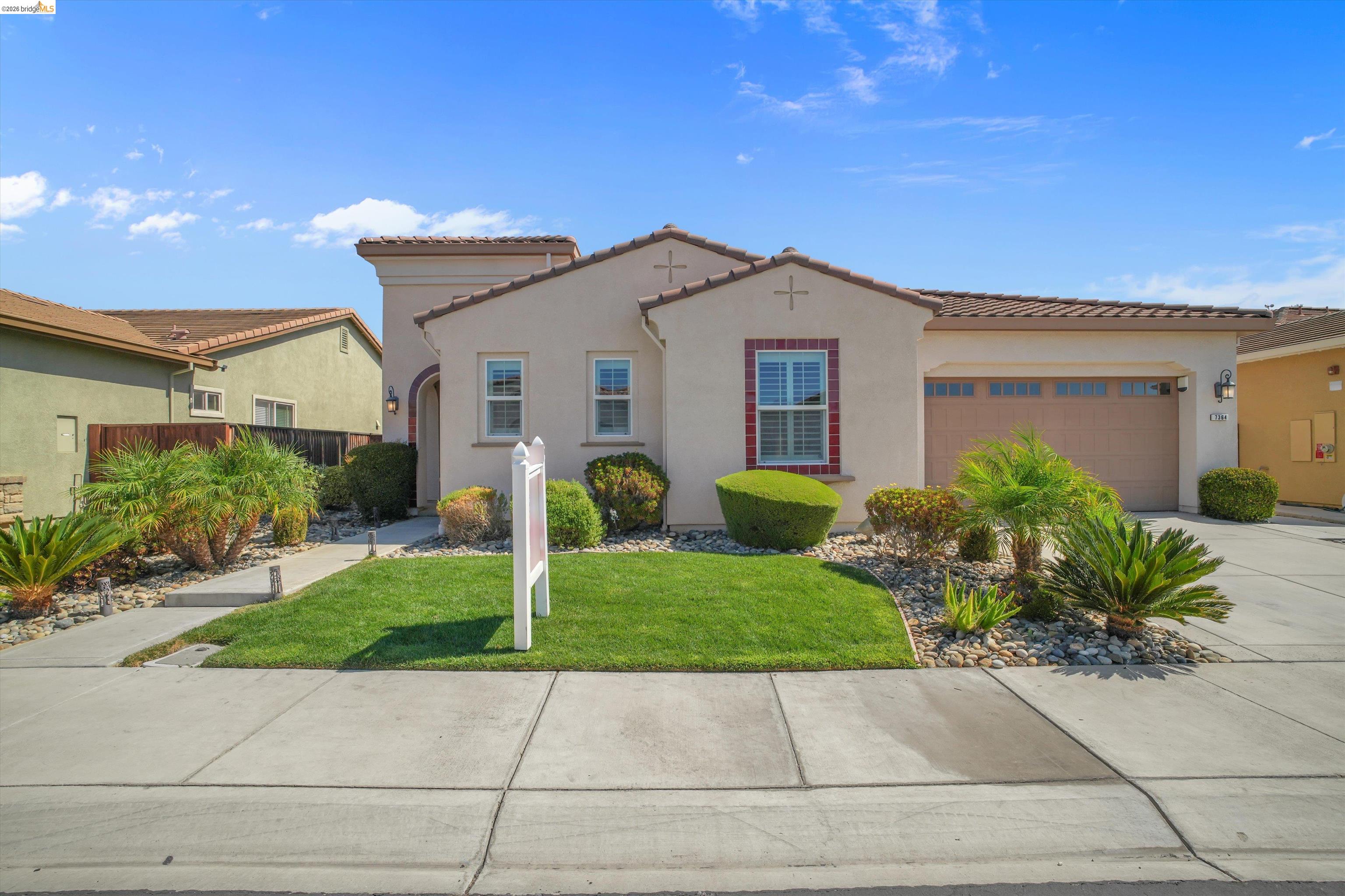 Stucco home with a two-car garage, red-trimmed window, and landscaped front lawn.