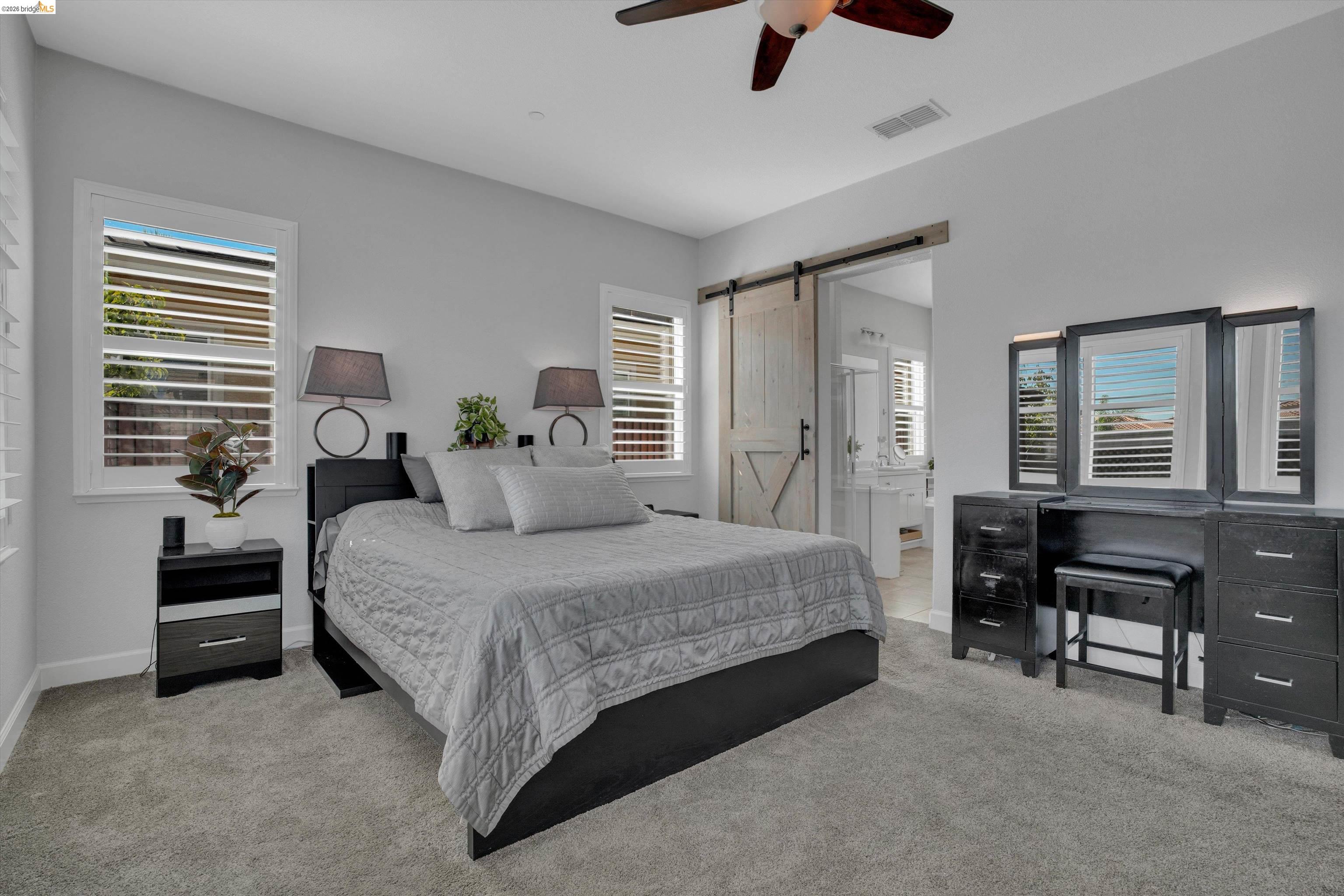 Primary bedroom with a gray upholstered bed, plantation shutters, and a barn-style sliding door.