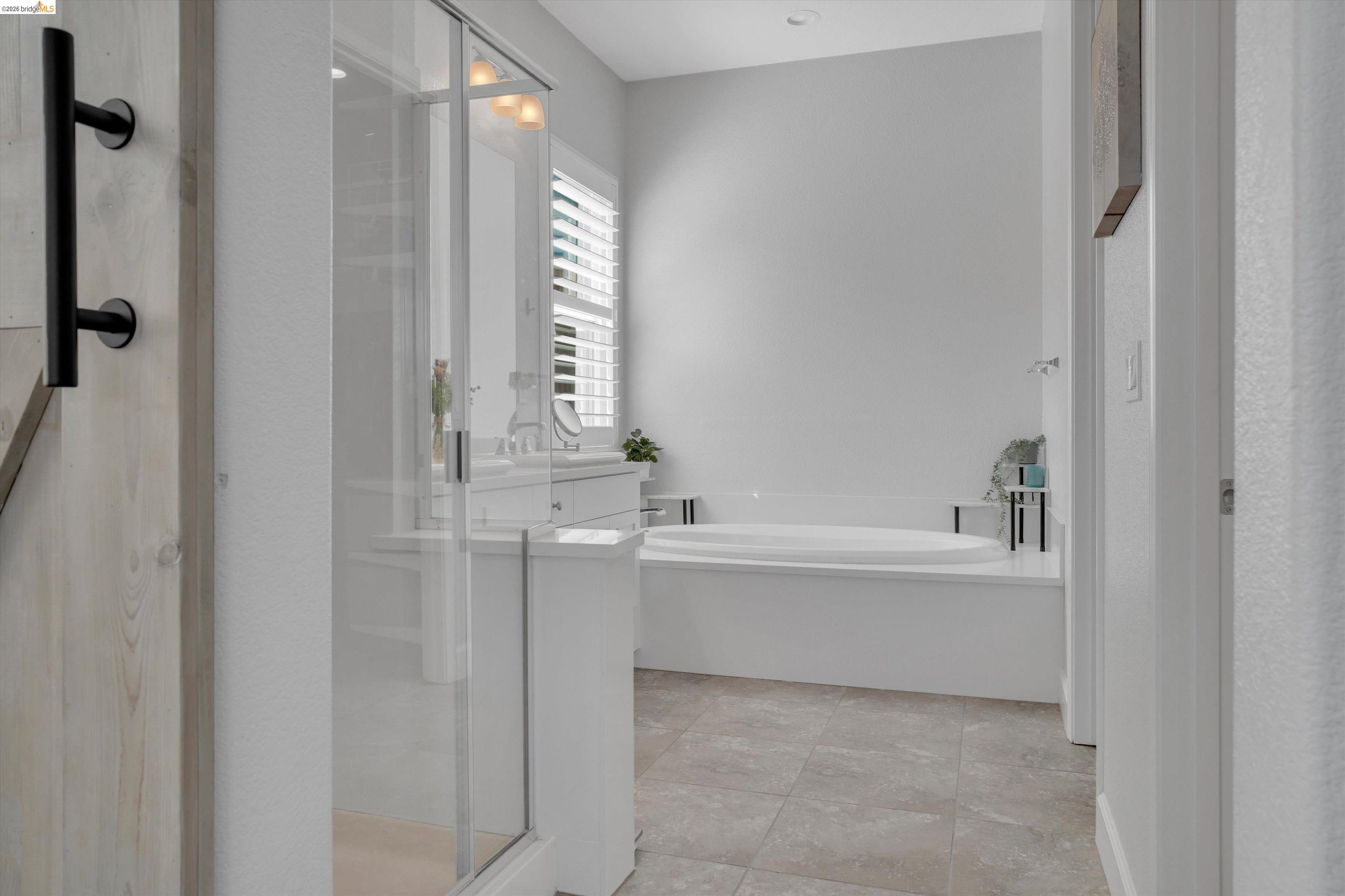 Bathroom with a glass shower, white vanity, and built-in soaking tub.