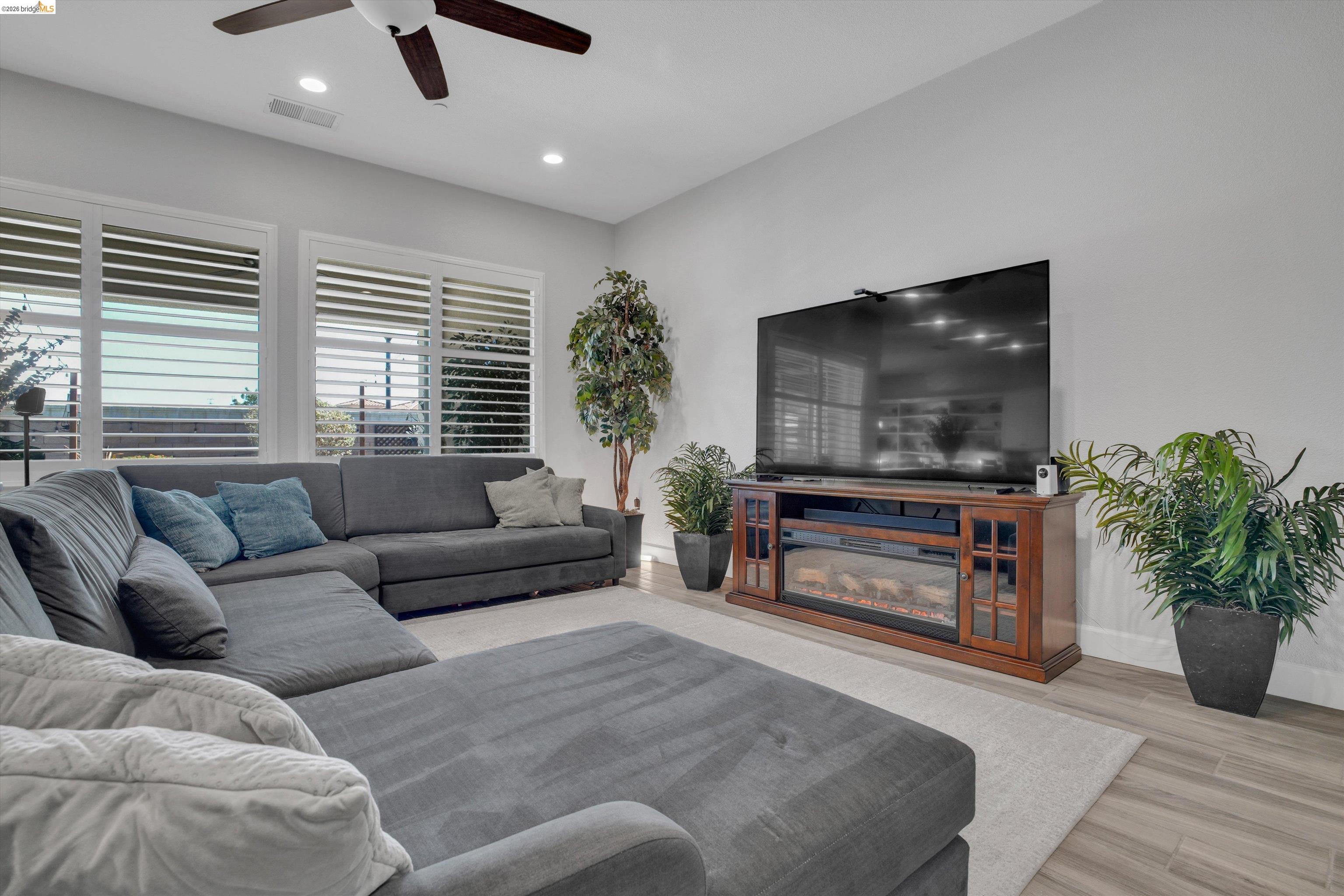 Living room with a large gray sectional, shuttered windows, and a TV above an electric fireplace.