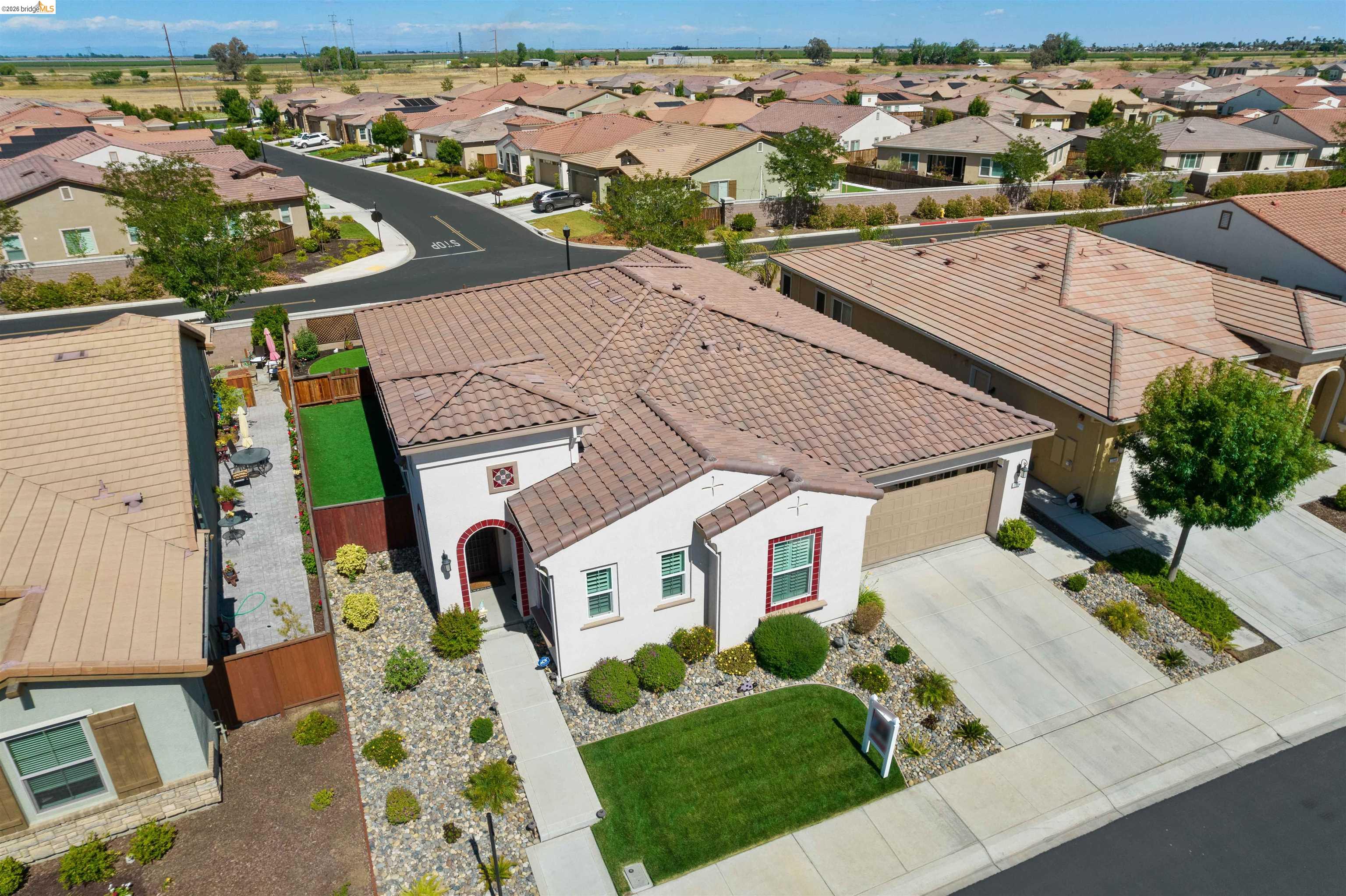 Aerial view of a stucco home with a tile roof, landscaped front yard, and fenced side patio.