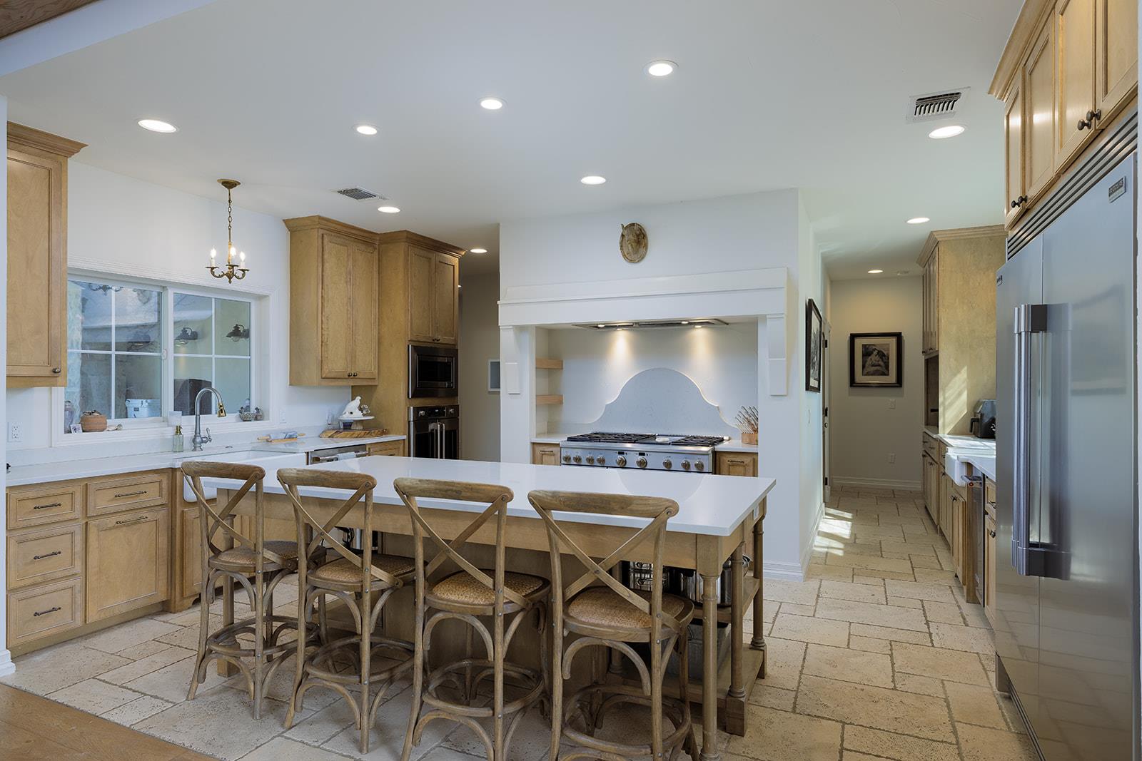Kitchen with a large island, light wood cabinets, and a white range hood over the range.