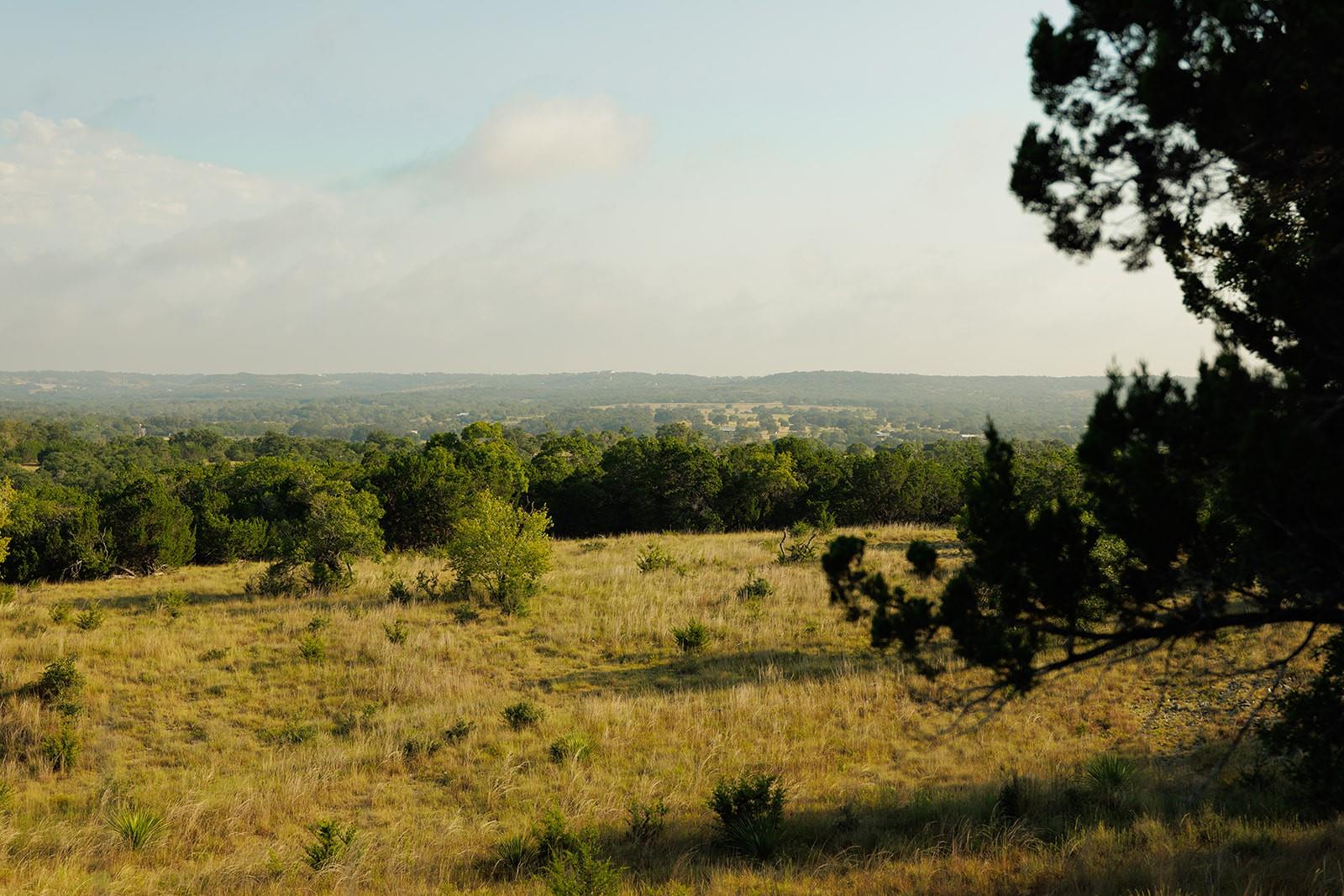 Open grassy acreage and wooded rolling hills framed by trees.