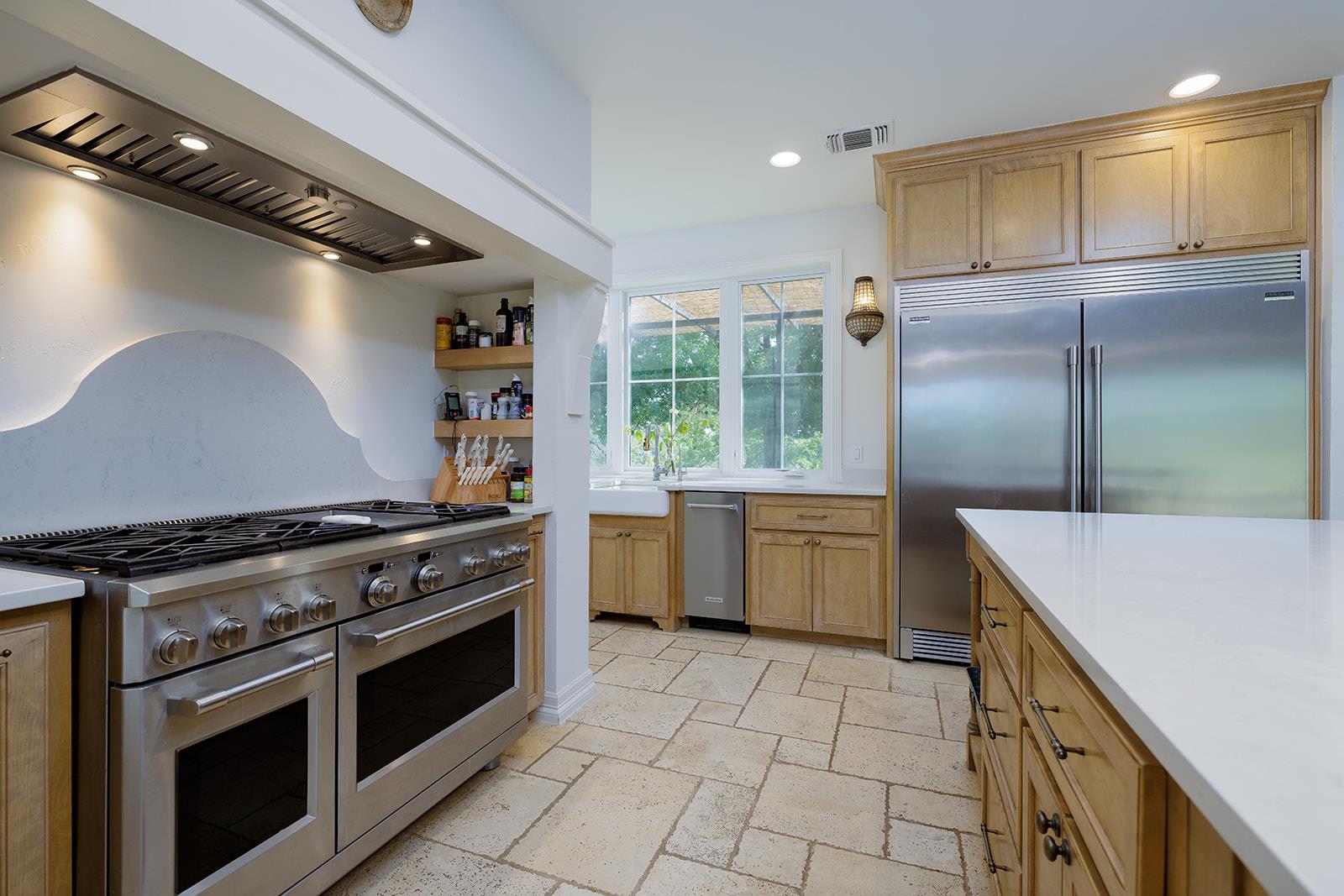 Kitchen with light wood cabinets, a large stainless range, side-by-side refrigerator, and farmhouse sink.