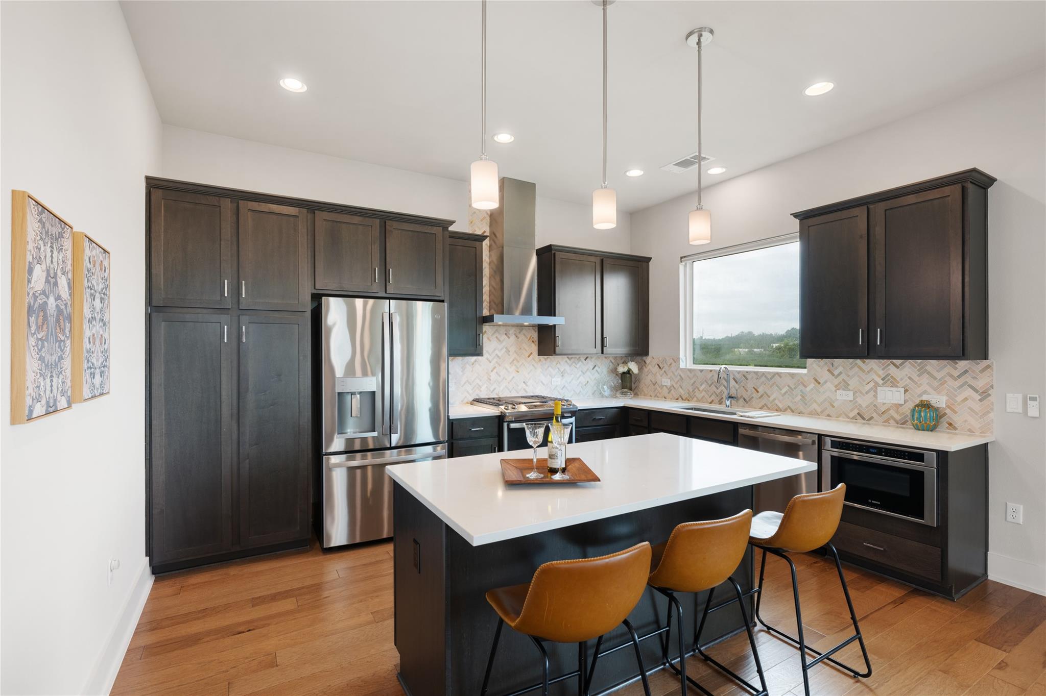 Kitchen with dark cabinetry, stainless appliances, and a white island lined with three mustard-colored stools.