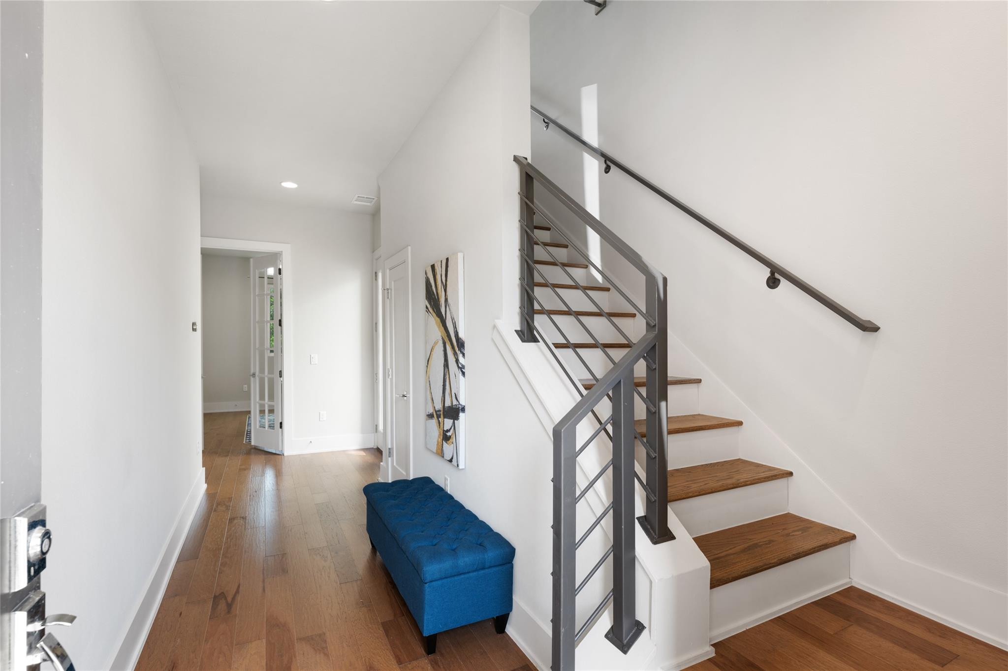 Entry hallway with a wood staircase, dark metal railing, and blue upholstered bench.