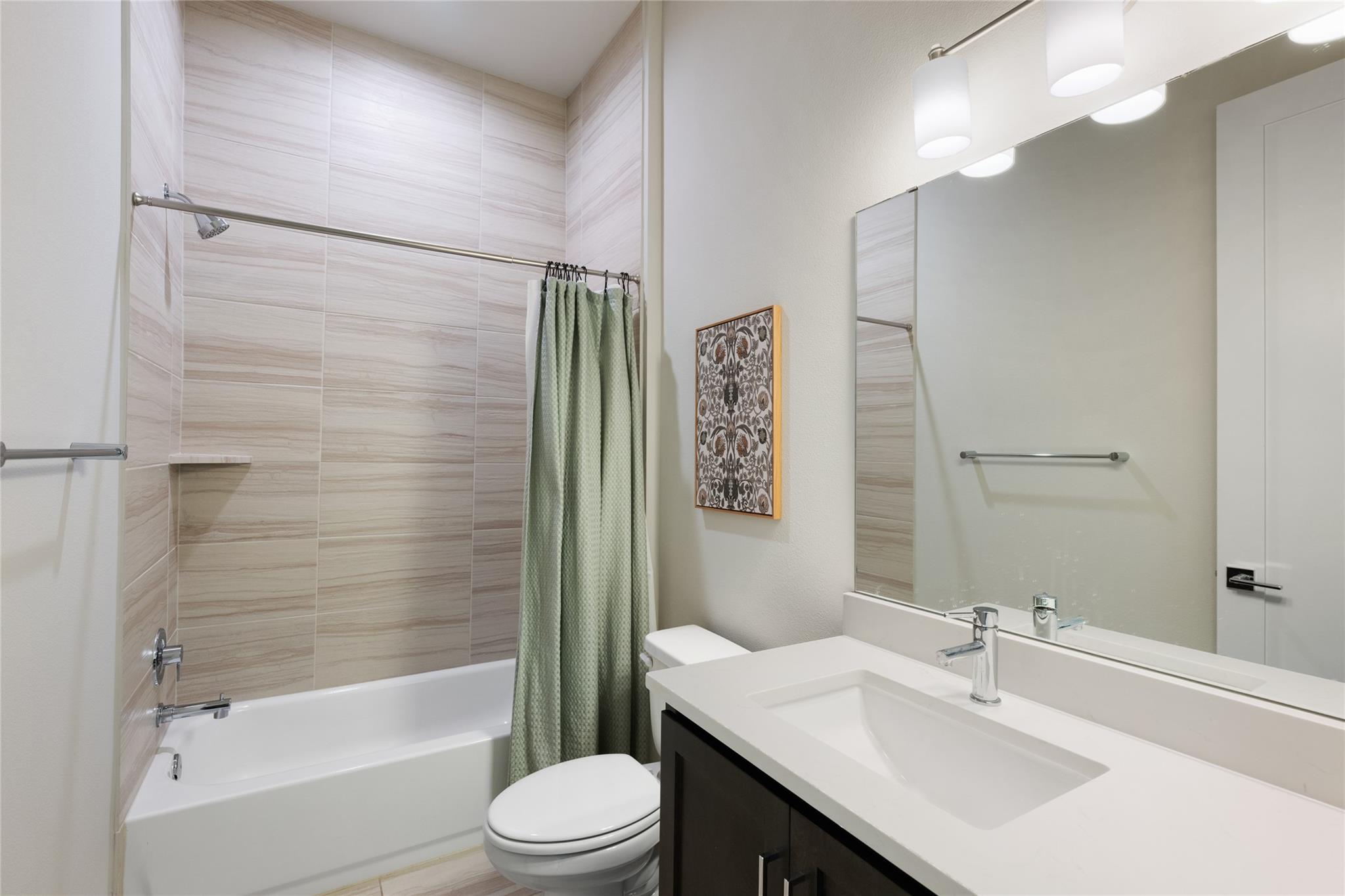 Bathroom with a tiled tub and shower, pale green curtain, and dark vanity with a white sink.