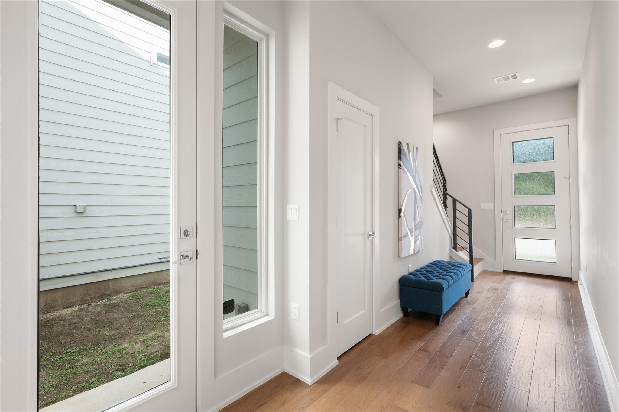 Entry foyer with a four-panel frosted-glass front door, black-railed stairs, and a blue tufted bench.