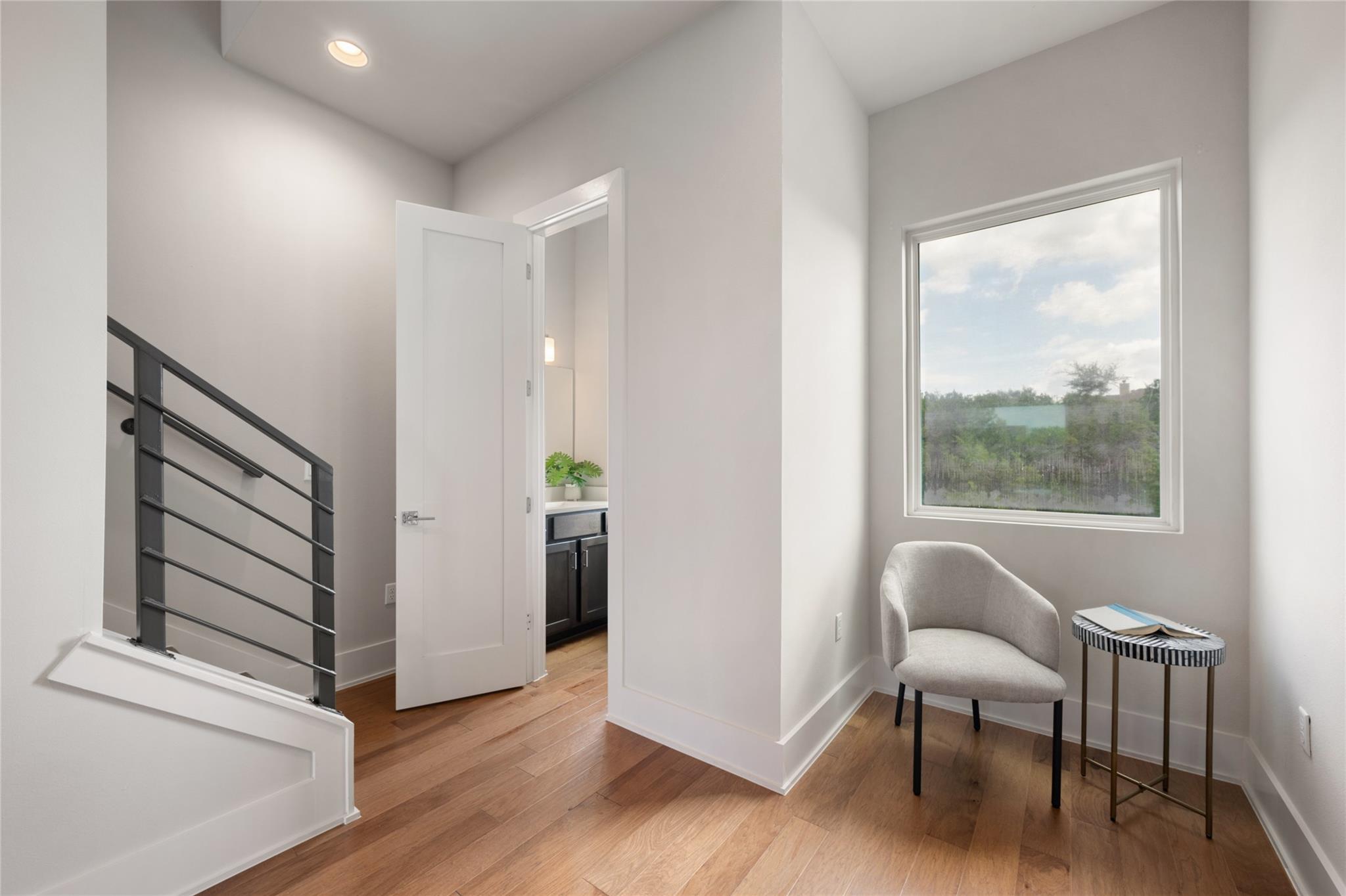 Upstairs landing with a metal stair railing, wood floors, and a chair beside a large window.