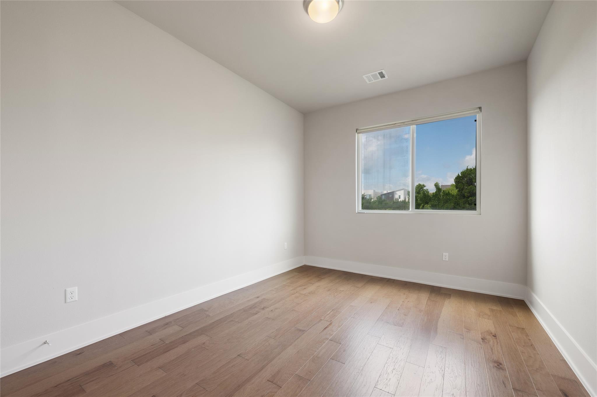 Vacant bedroom with light wood floors and a window overlooking trees.