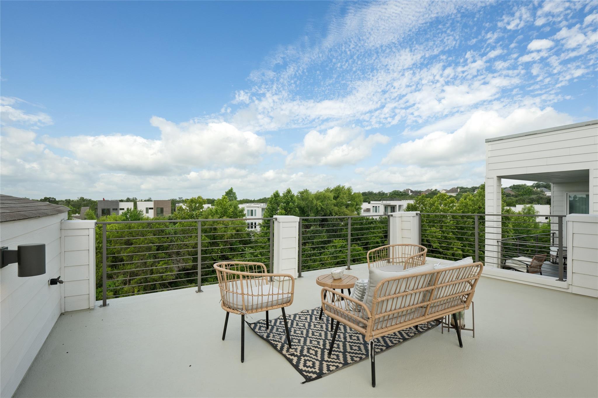 Furnished rooftop deck with wicker seating and treetop views.