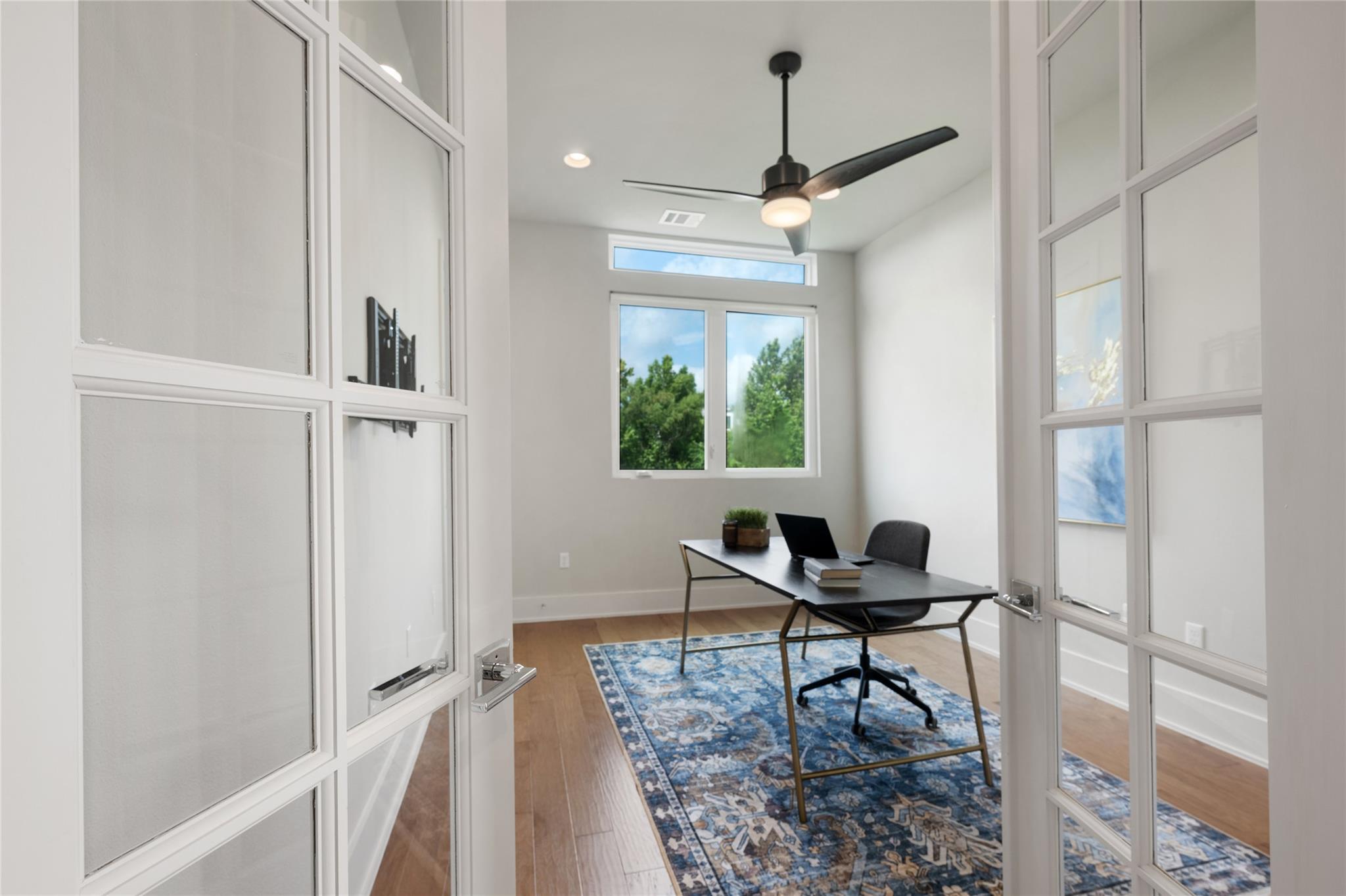 Staged home office with a black desk on a blue patterned rug, seen through glass-paneled doors.
