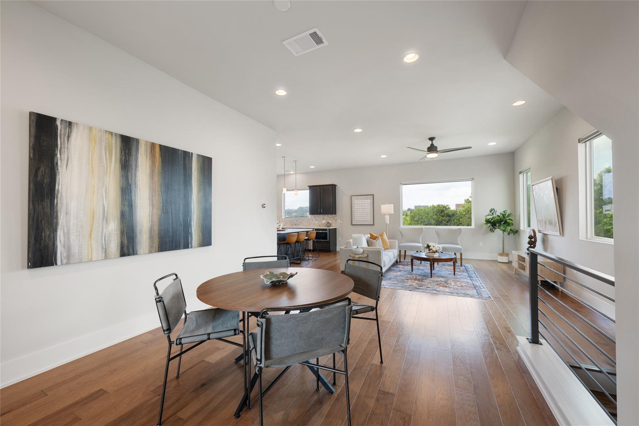 Open-plan dining and living area with a round wood table, gray chairs, and large abstract wall art.