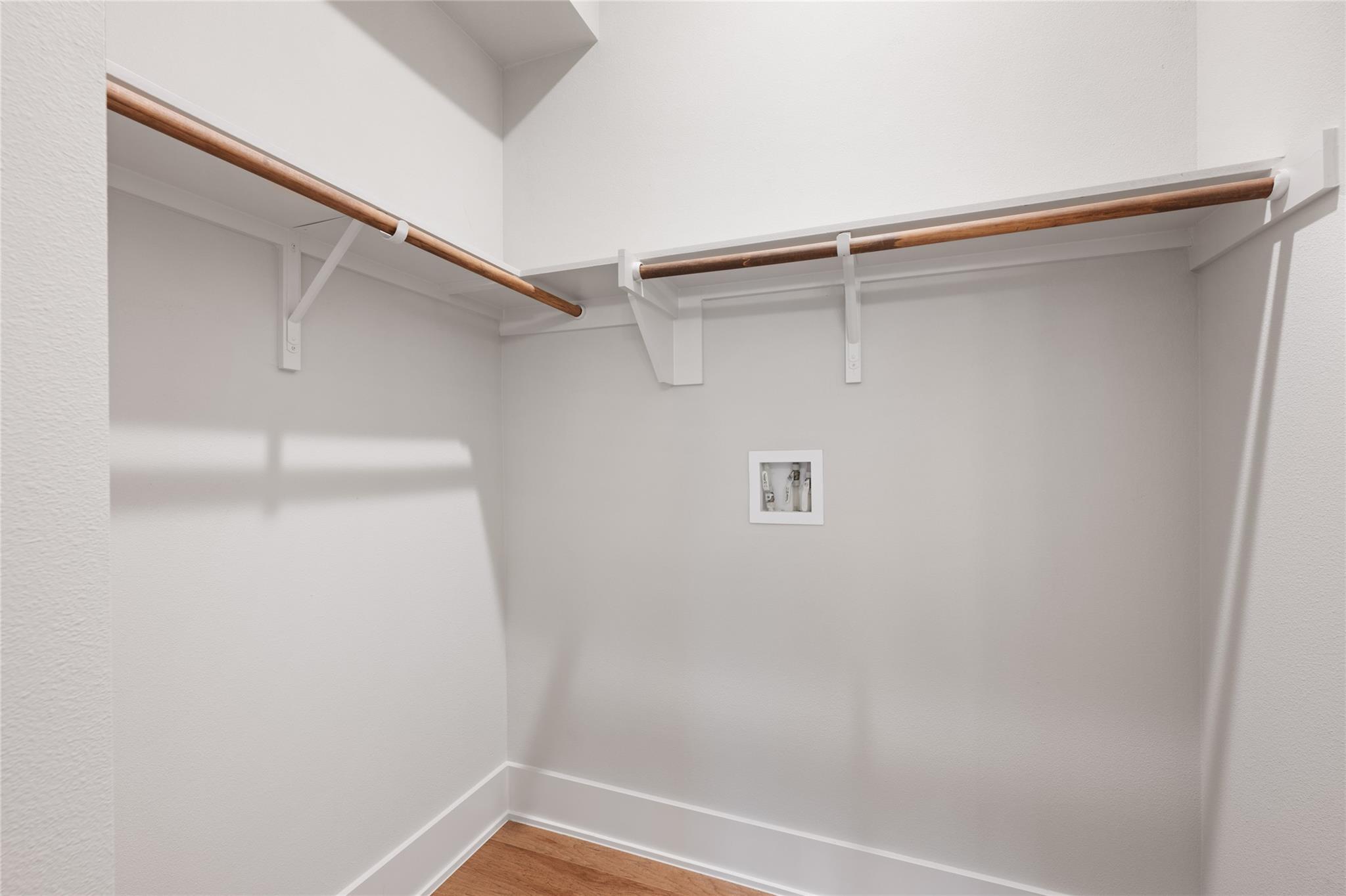Empty walk-in closet with wooden hanging rods, white shelves, and hardwood flooring.