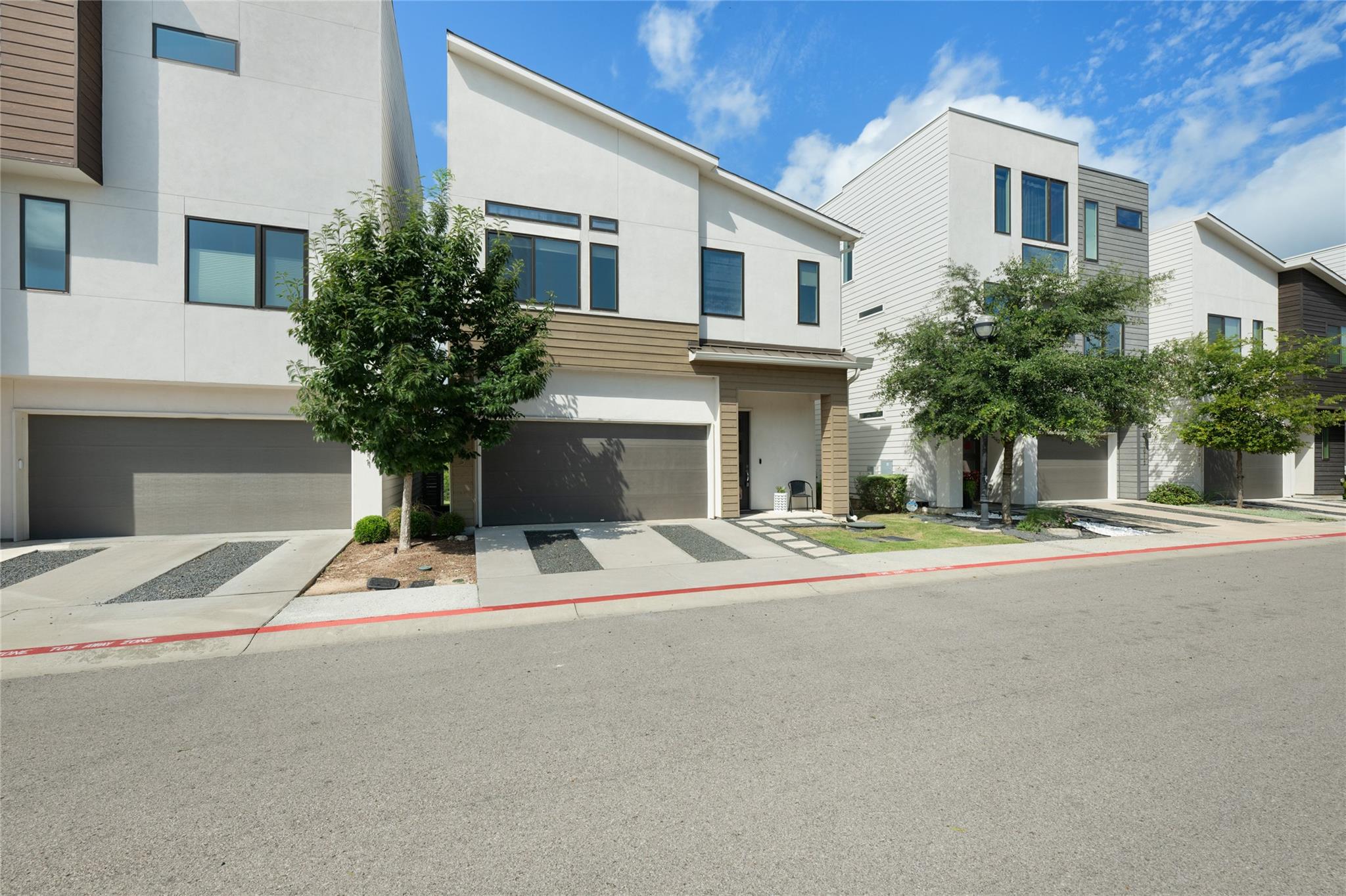 Modern multi-story home with light siding, a dark garage door, and trees along the street.