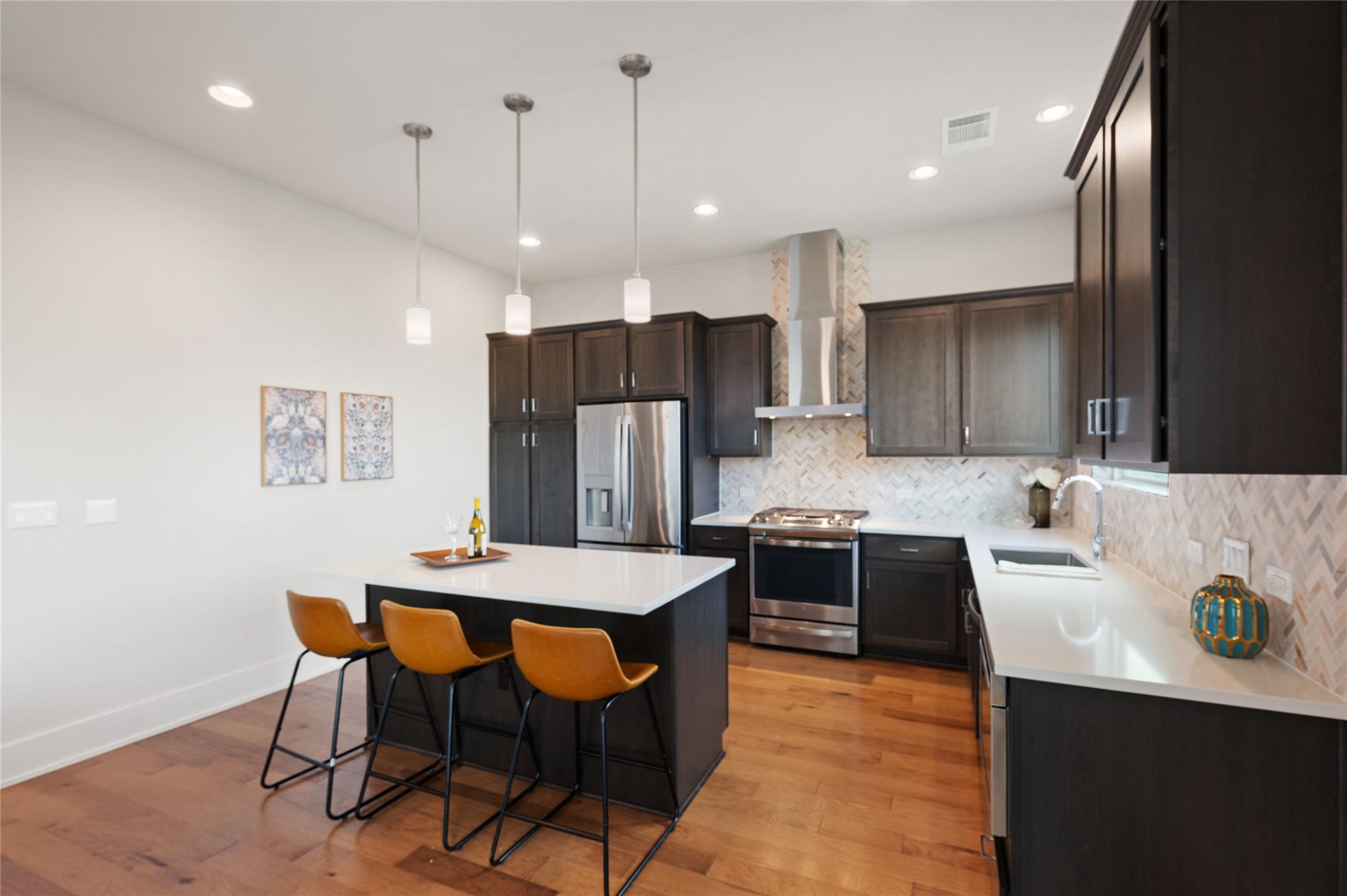 Kitchen with dark wood cabinets, stainless steel appliances, and a white island with three bar stools.