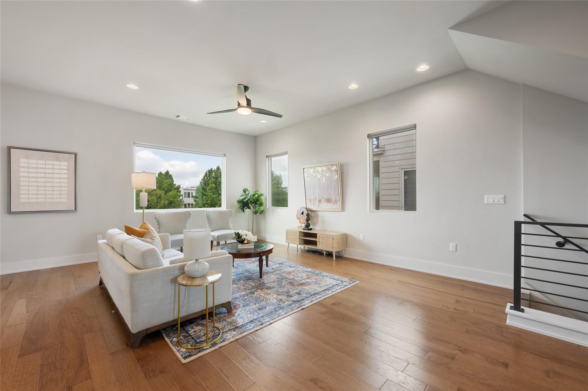Furnished living room with a white sofa, patterned rug, wood floors, and large windows.